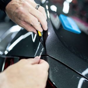 A close up of a person cutting a piece of tape on a car.