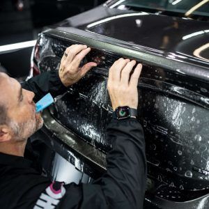 A man is applying a protective film to the back of a car.