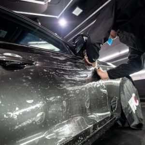 A man is applying a protective film to the side of a car.