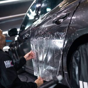 A man is applying a clear film to the side of a car.