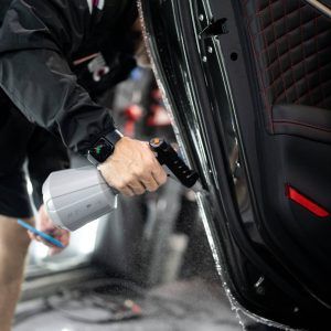 A man is spraying a car door with a spray bottle.