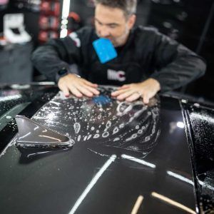 A man is applying a protective film to the roof of a car.
