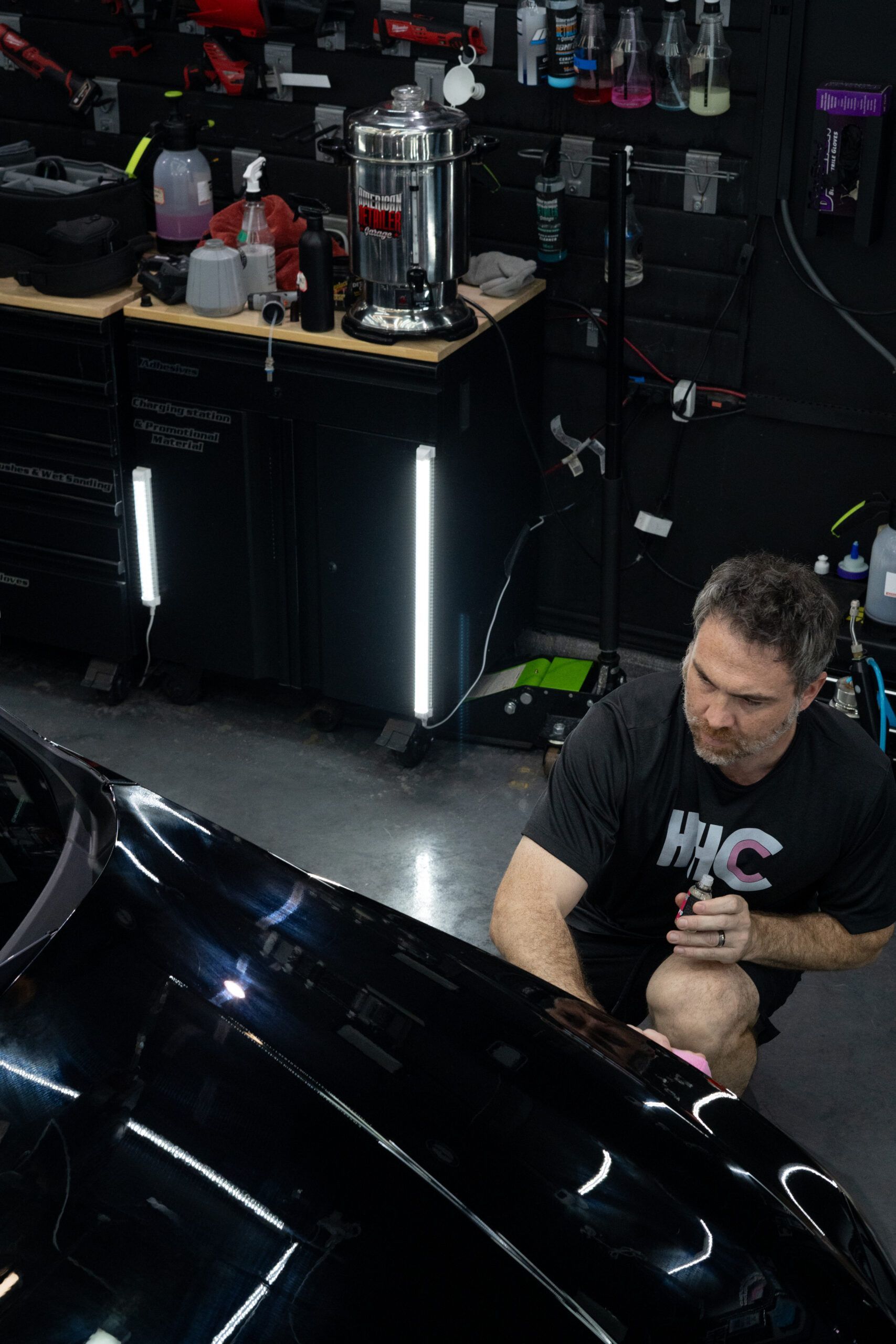 A man is sitting next to a black car in a garage.