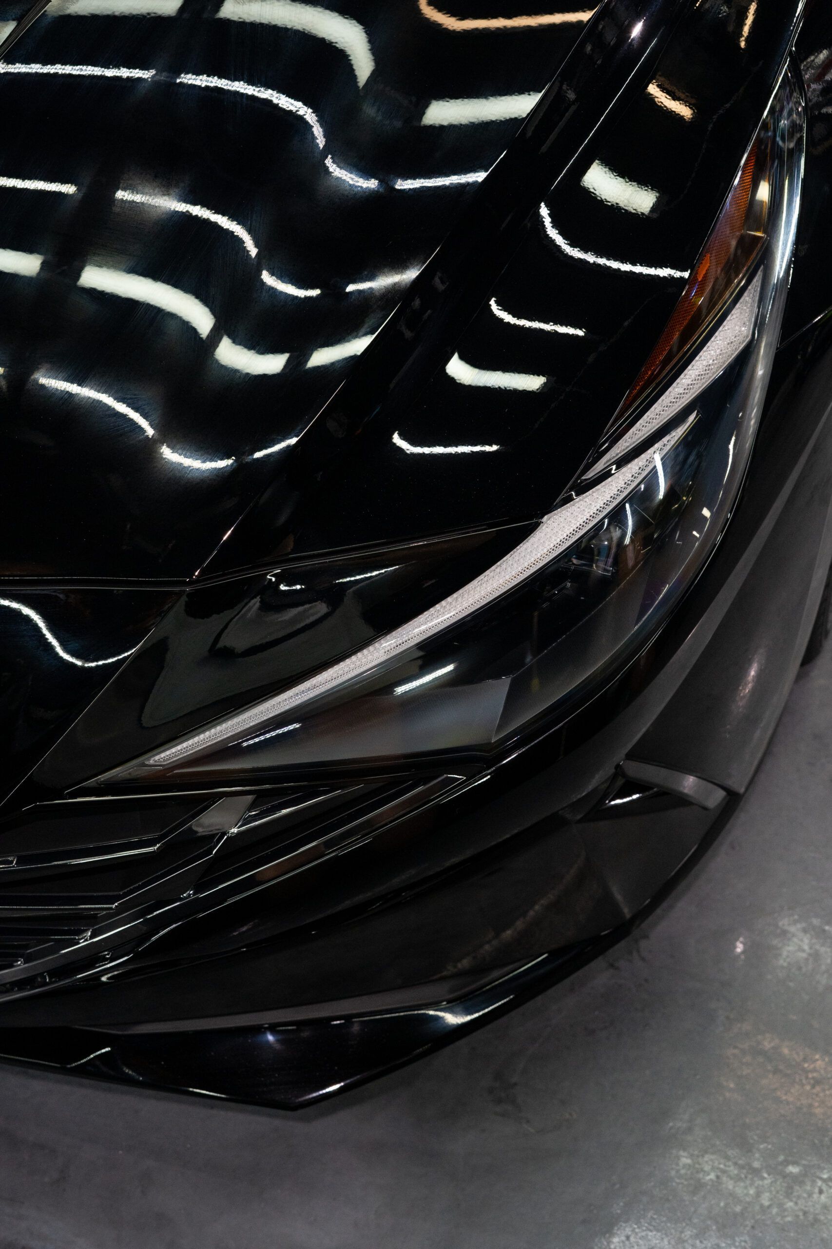 A close up of a black car 's headlight and hood