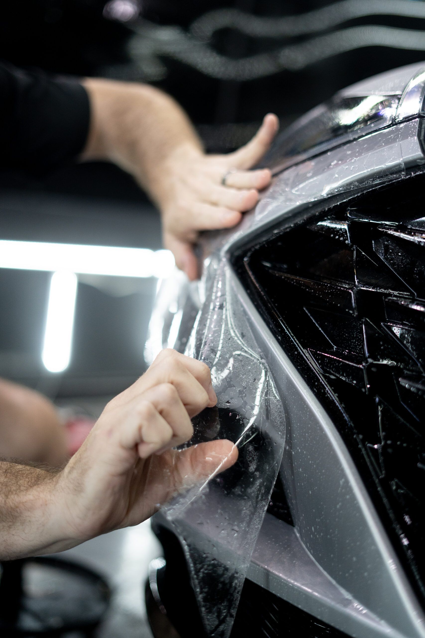 A person is applying a protective film to the front of a car.