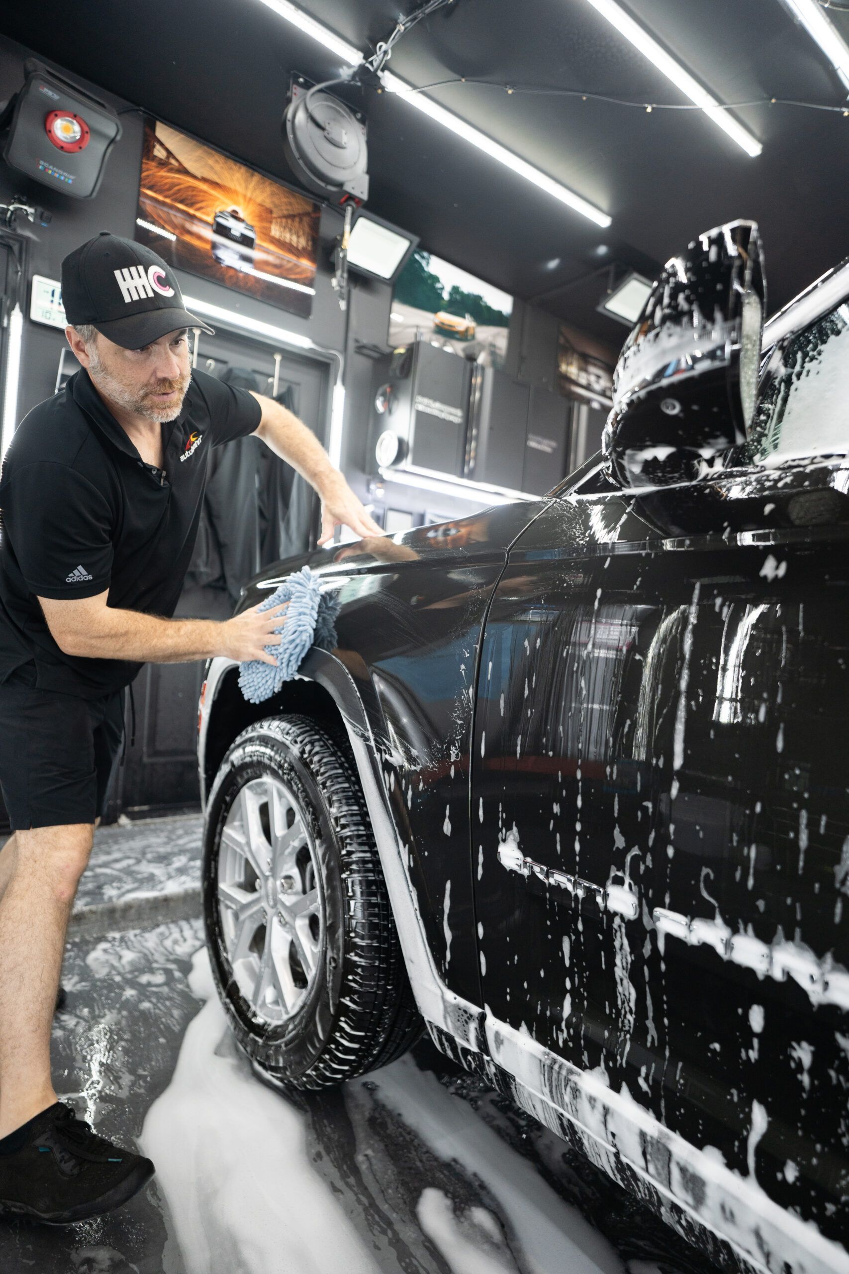 A man is washing a black car in a garage.