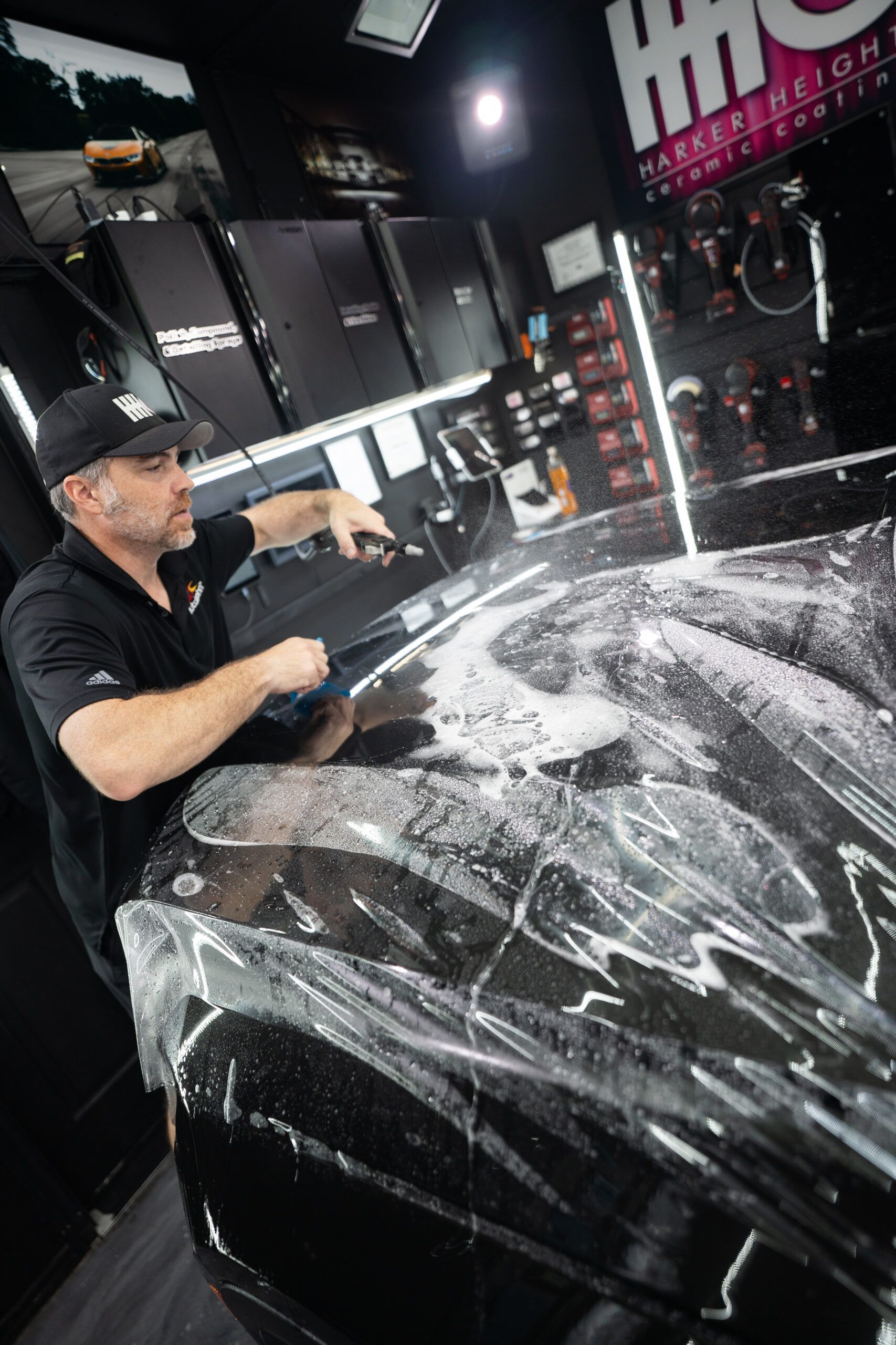 A man is wrapping a black car with plastic wrap.