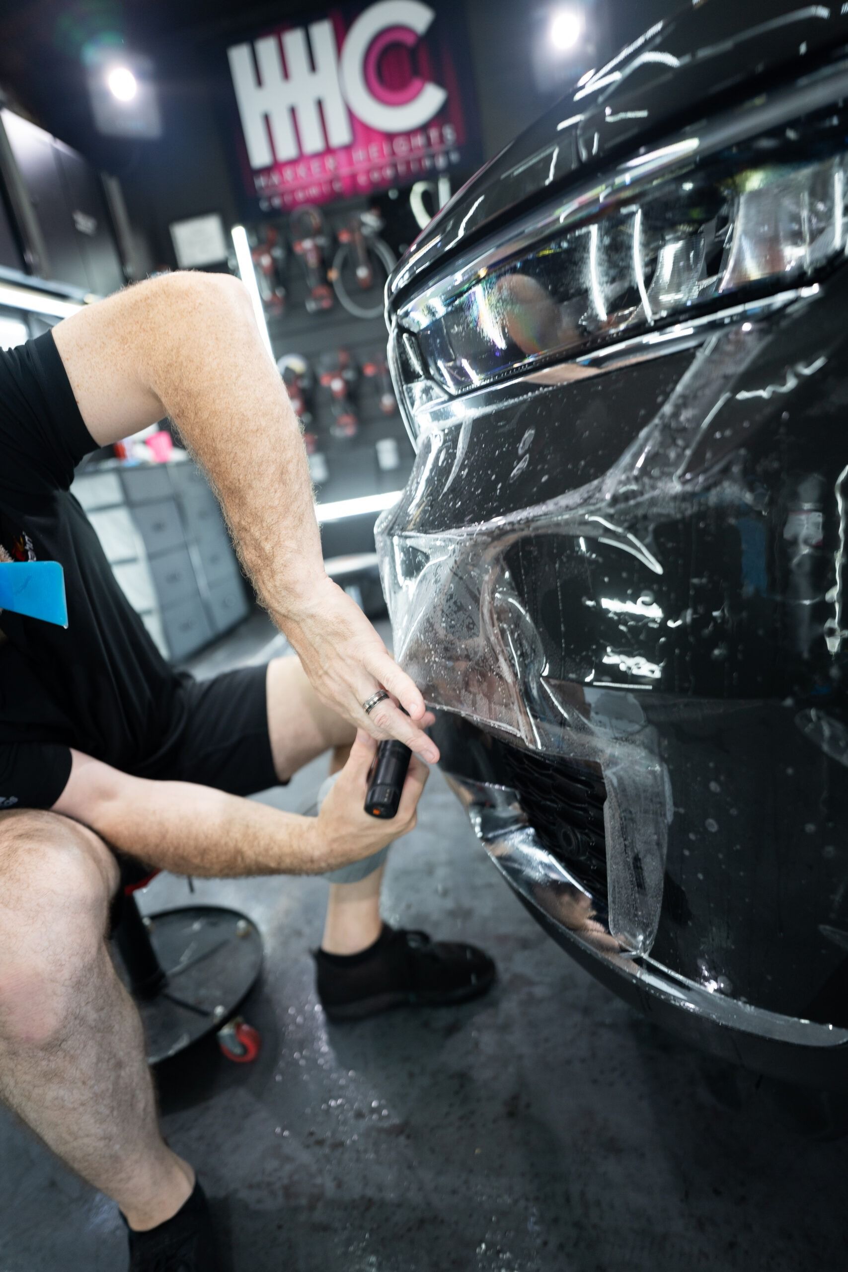 A man is applying a protective film to the front bumper of a car.