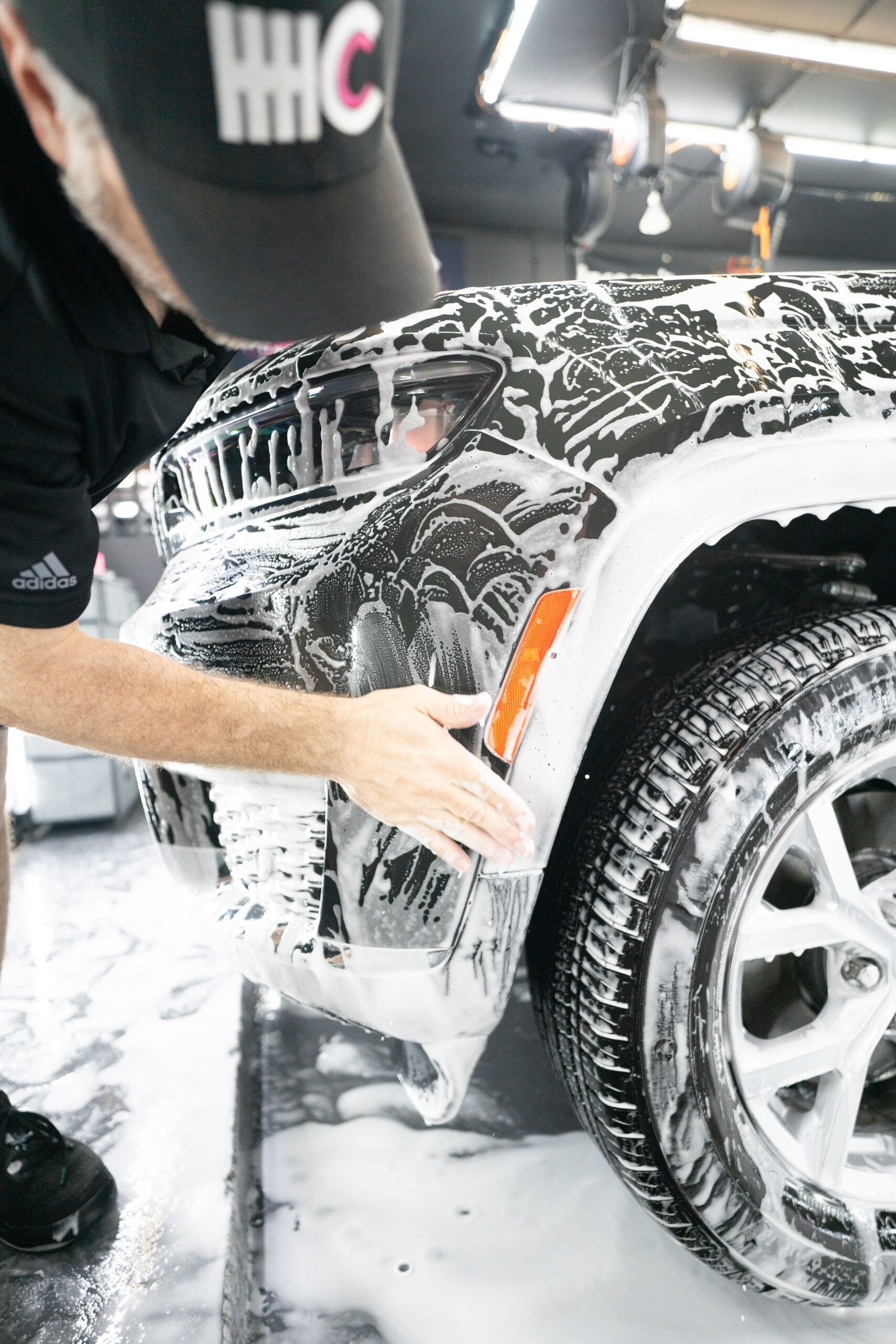 A man in a hat is washing a car with foam.