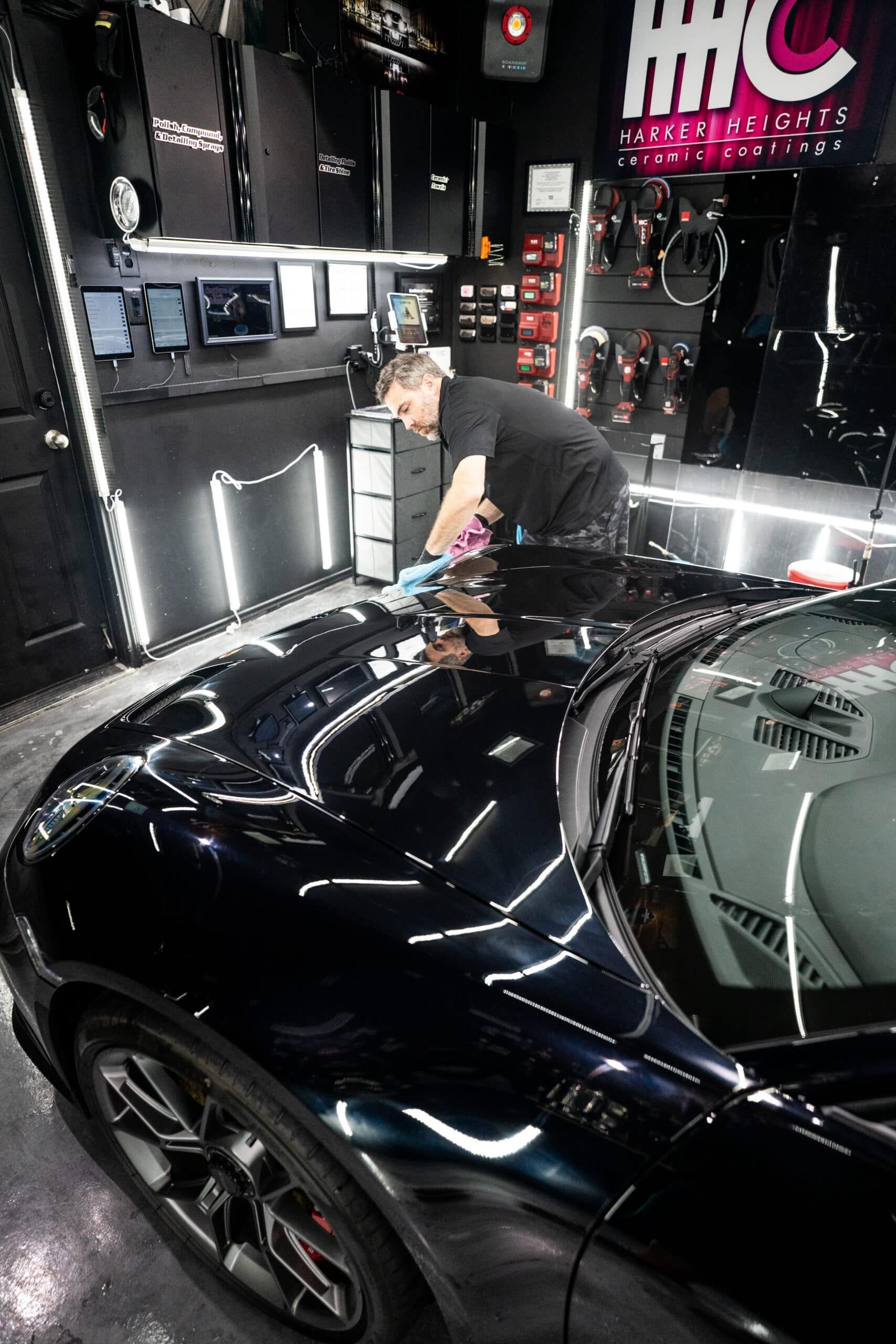 A man is polishing the hood of a black car in a garage.