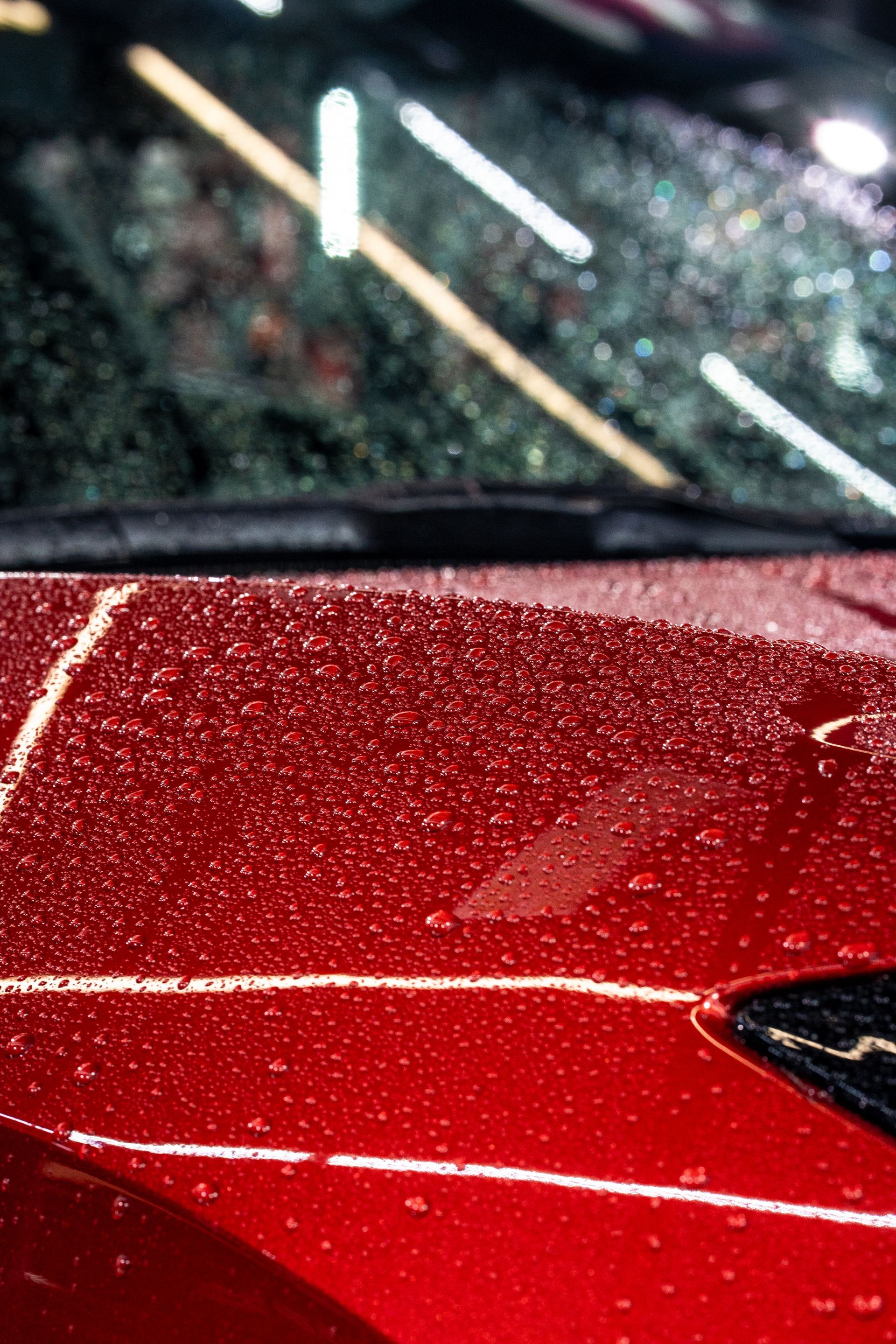 A close up of a red car with water drops on the hood.