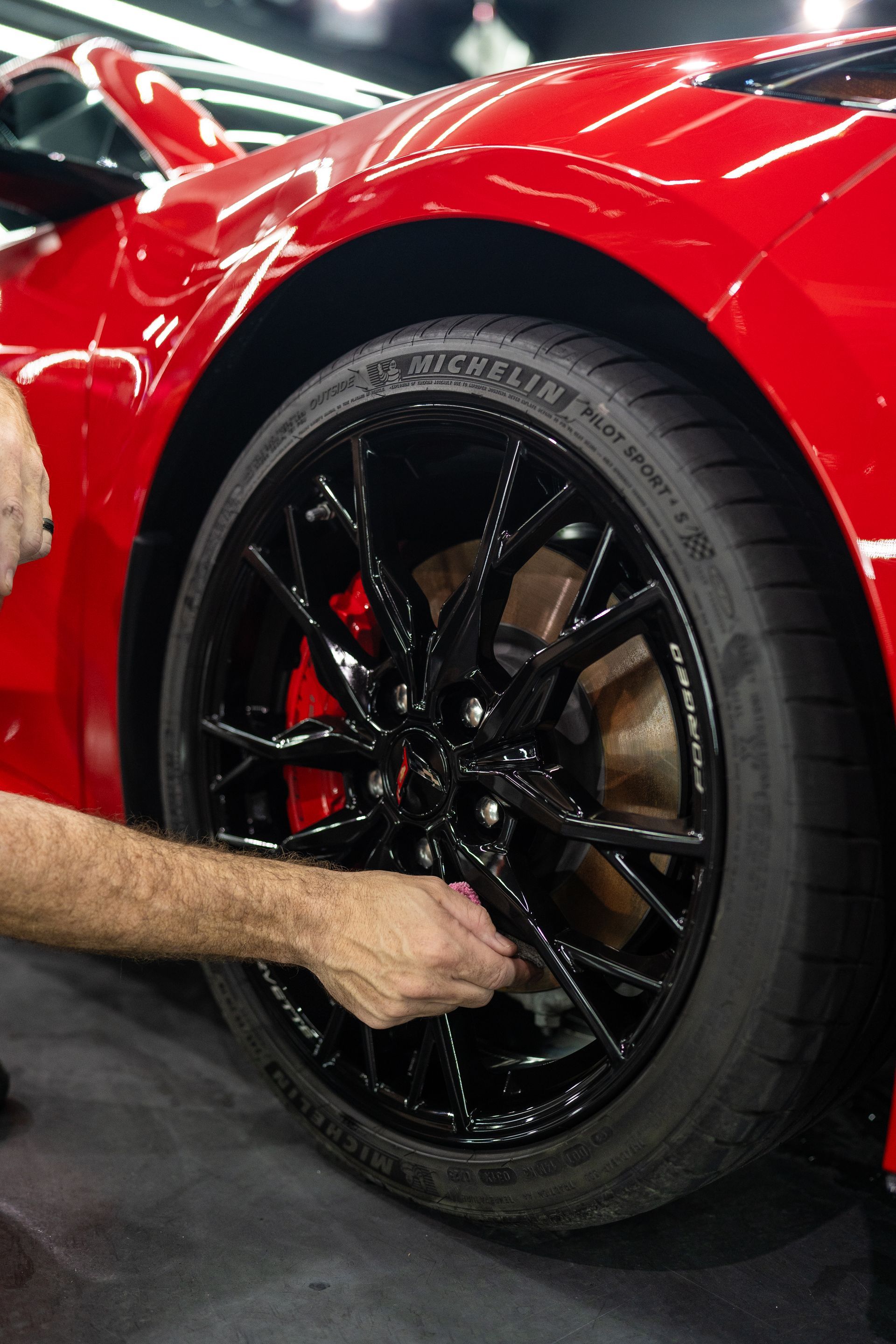A man is cleaning the wheels of a red sports car