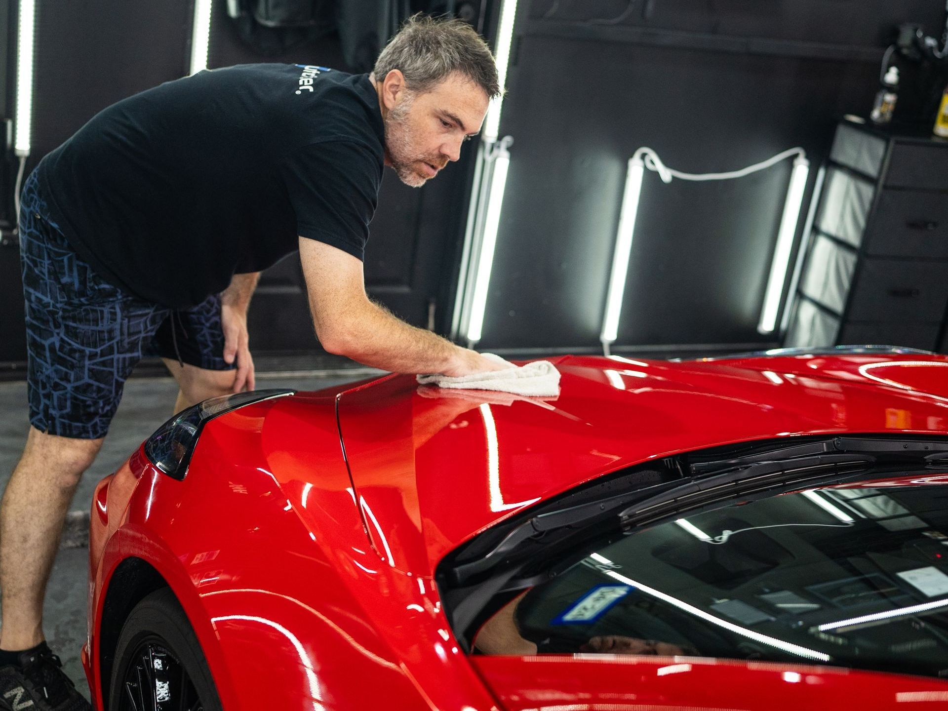 A man is cleaning a red sports car with a cloth.