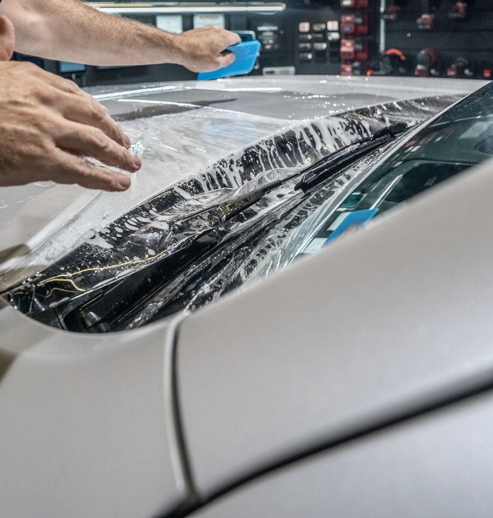 A man is installing a paint protection film on the hood of a white car.