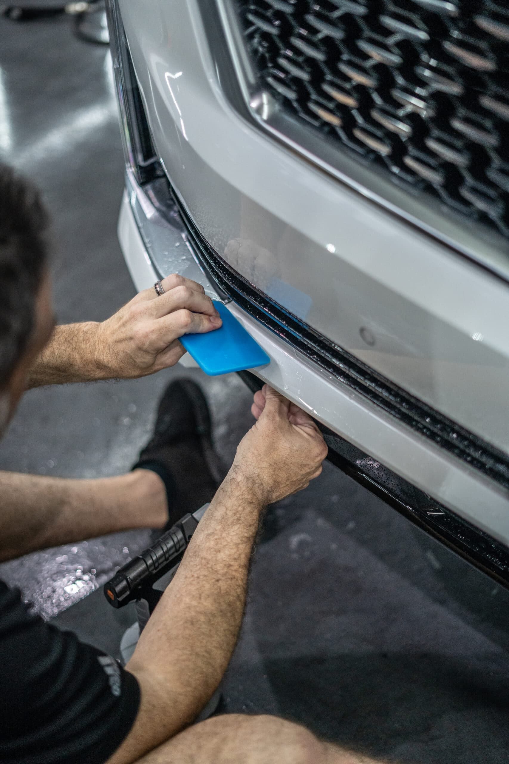 A man is applying a protective film to the front bumper of a car.
