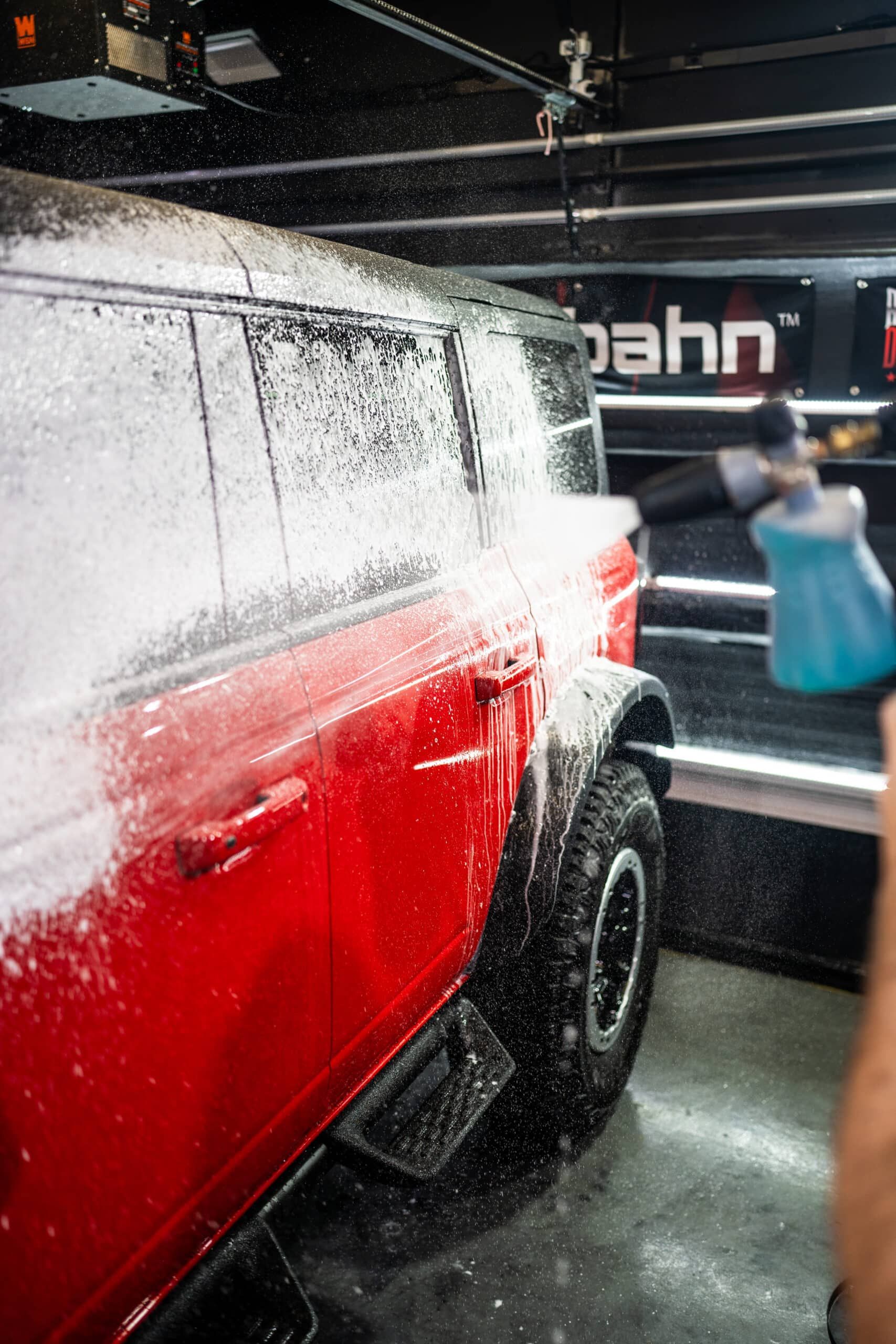 A red suv is being washed with foam in a garage.