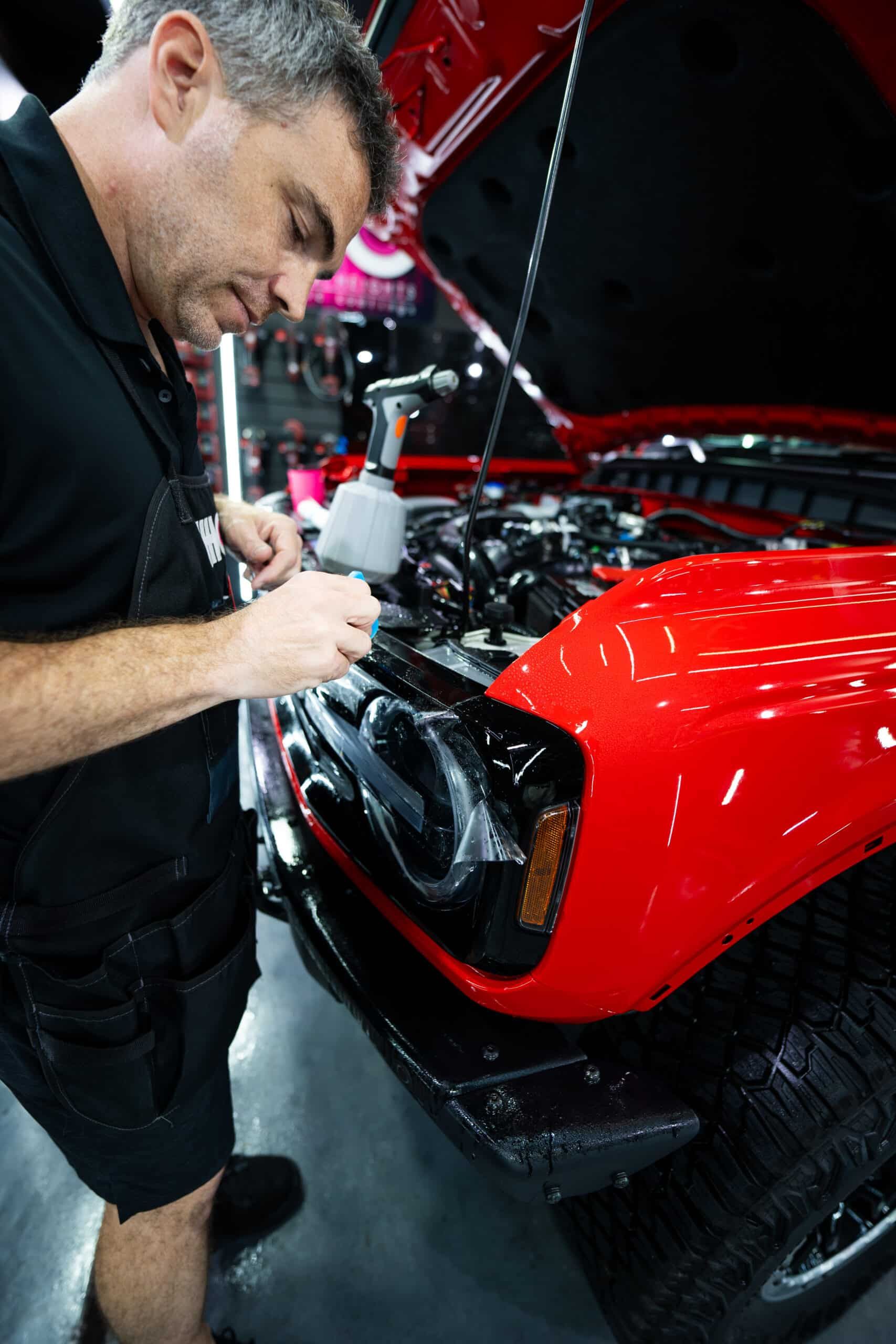 A man is working on a red car with the hood open
