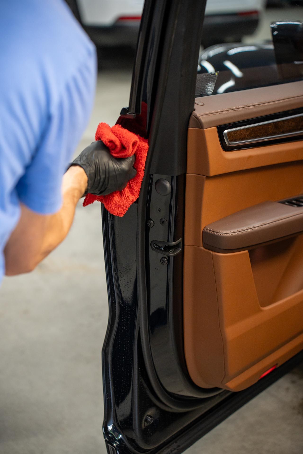 Person in black gloves wiping car door frame with red cloth. Interior with brown and black accents.