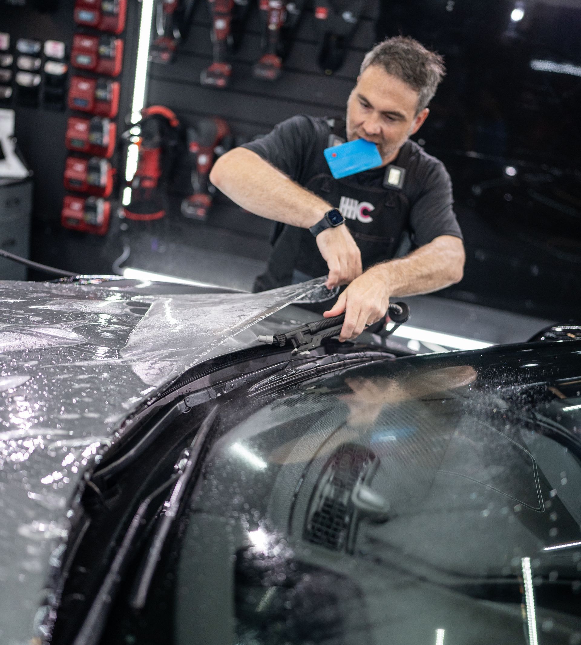 A man is cleaning the windshield of a car in a garage.
