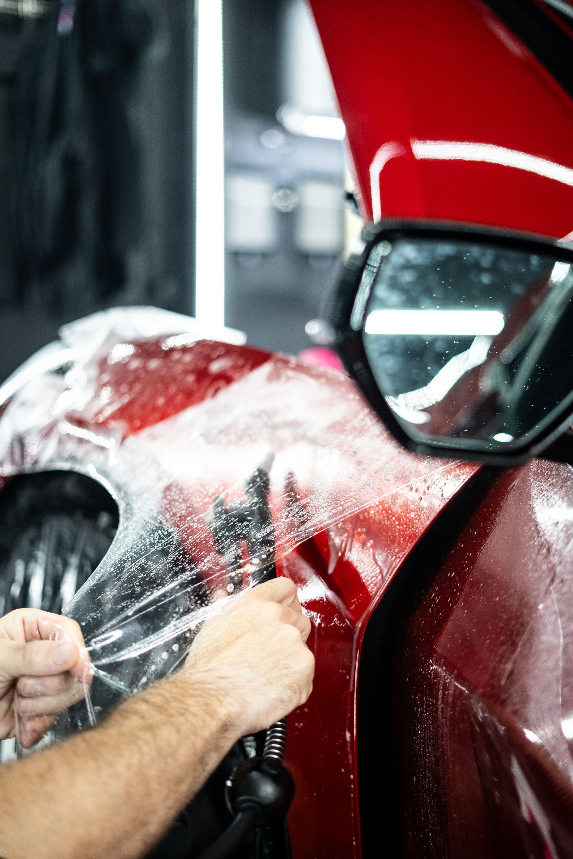 A man is wrapping a red car with plastic wrap.