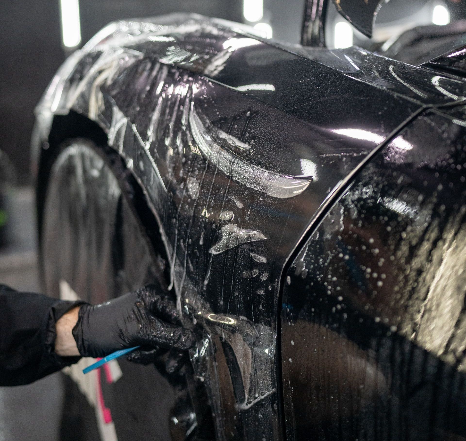 A person is cleaning the side of a black car with a brush.