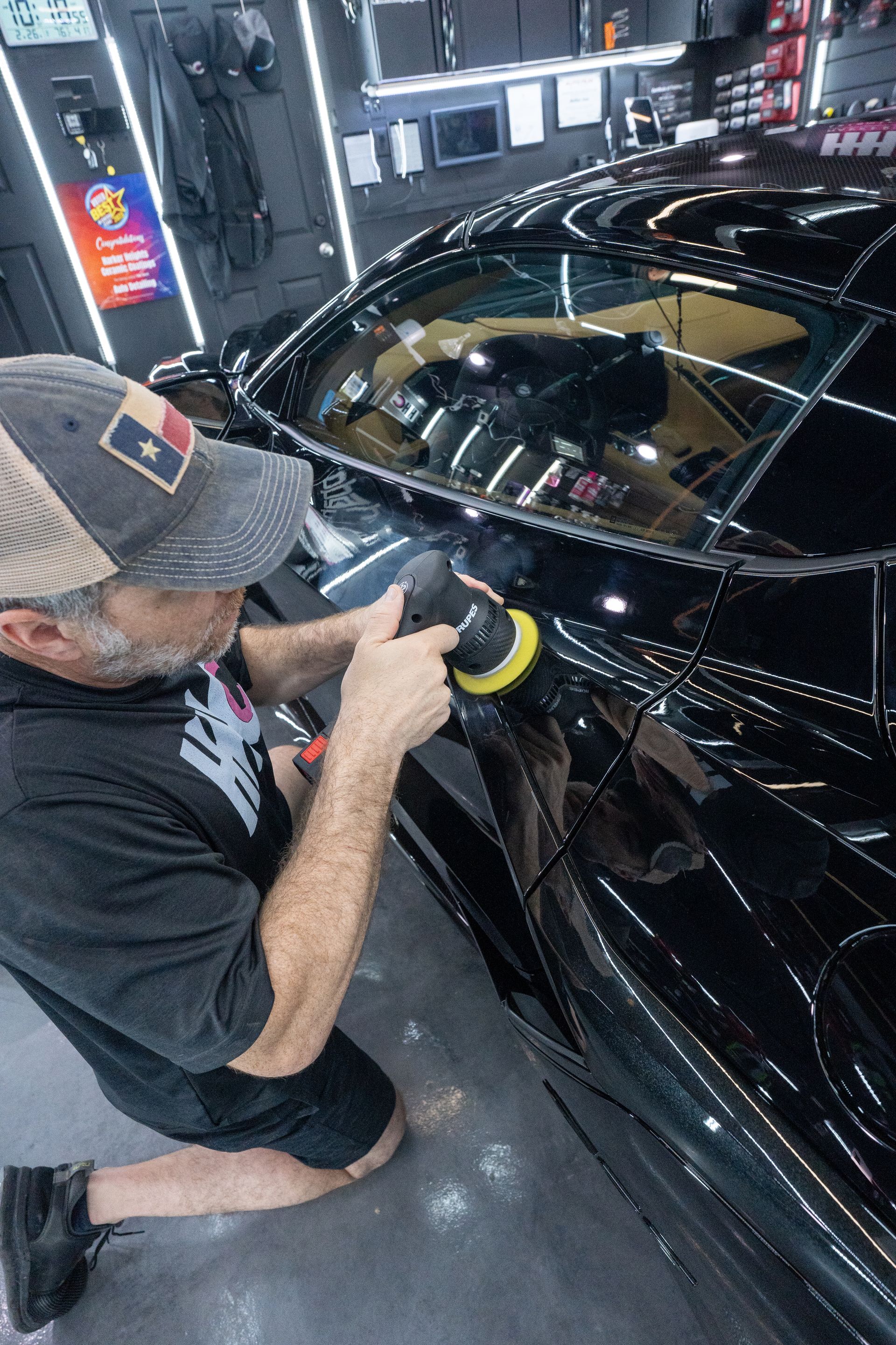 A man is polishing a black car in a garage.