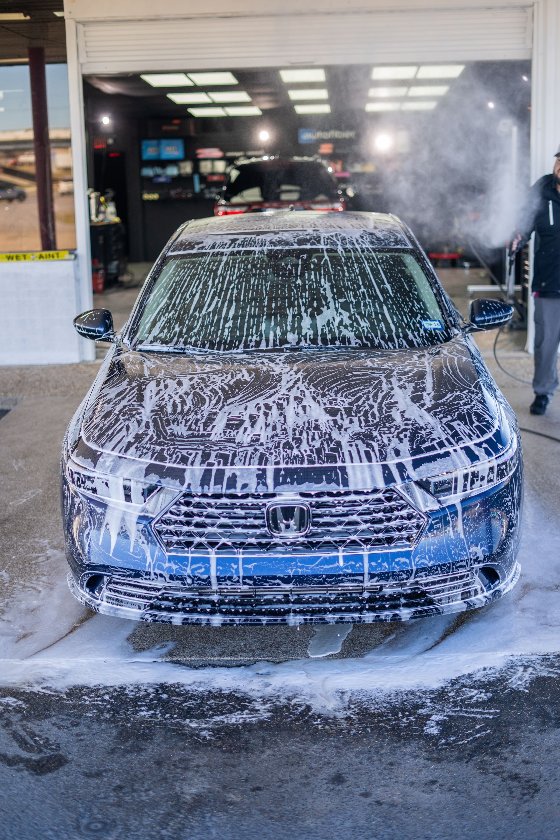Blue car being covered in soapy foam at a car wash.