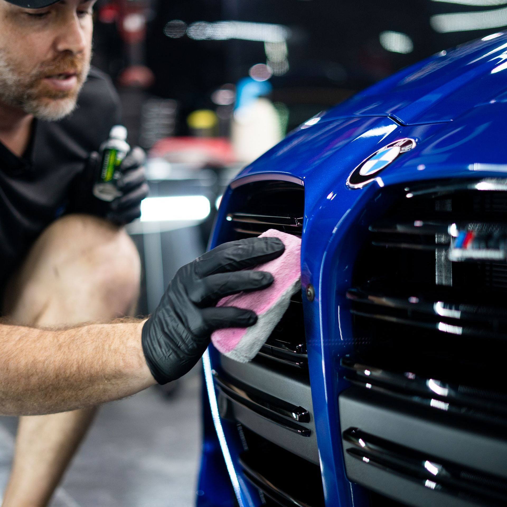 A man is polishing a red sports car in a garage.