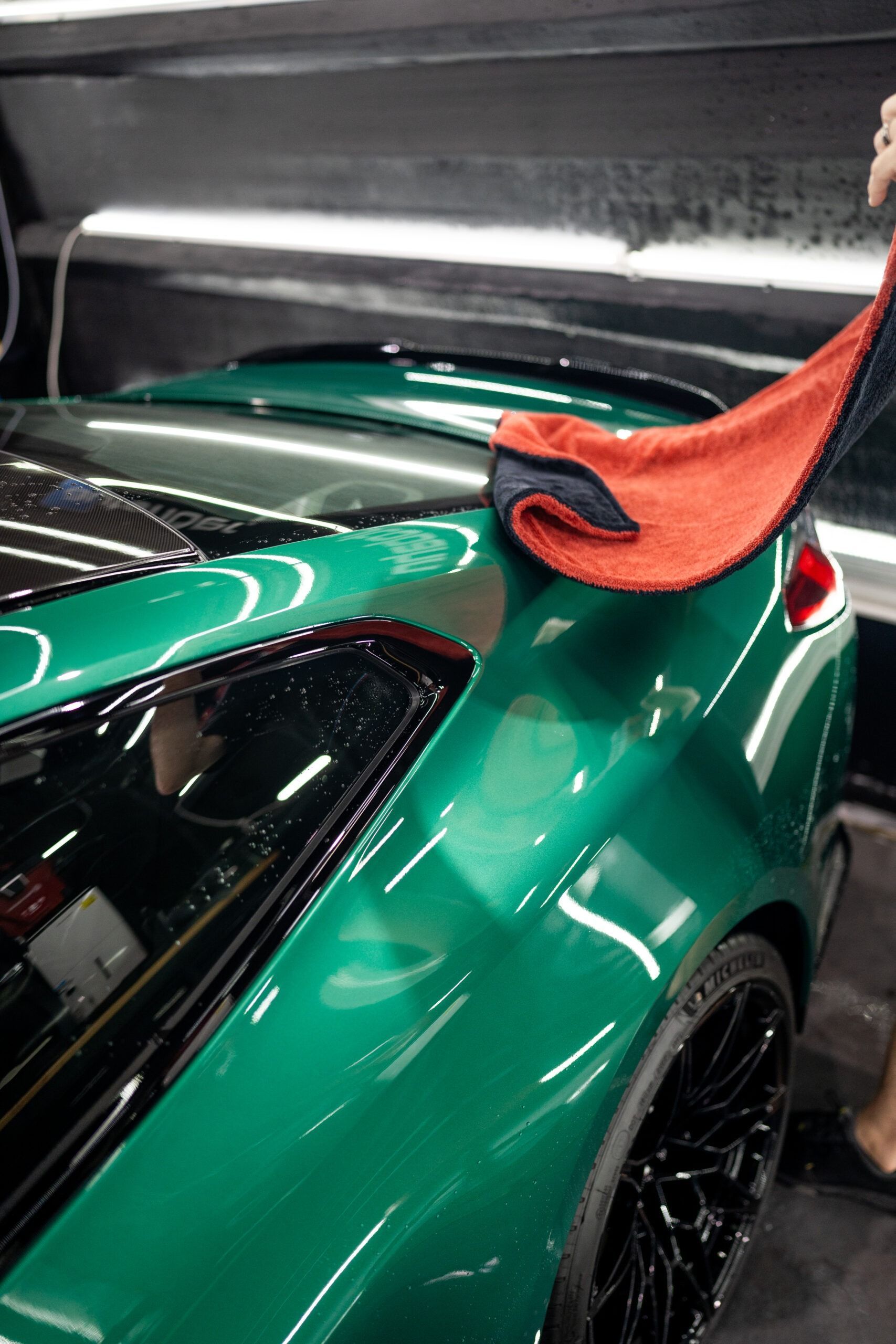 A person is cleaning a green sports car with a towel