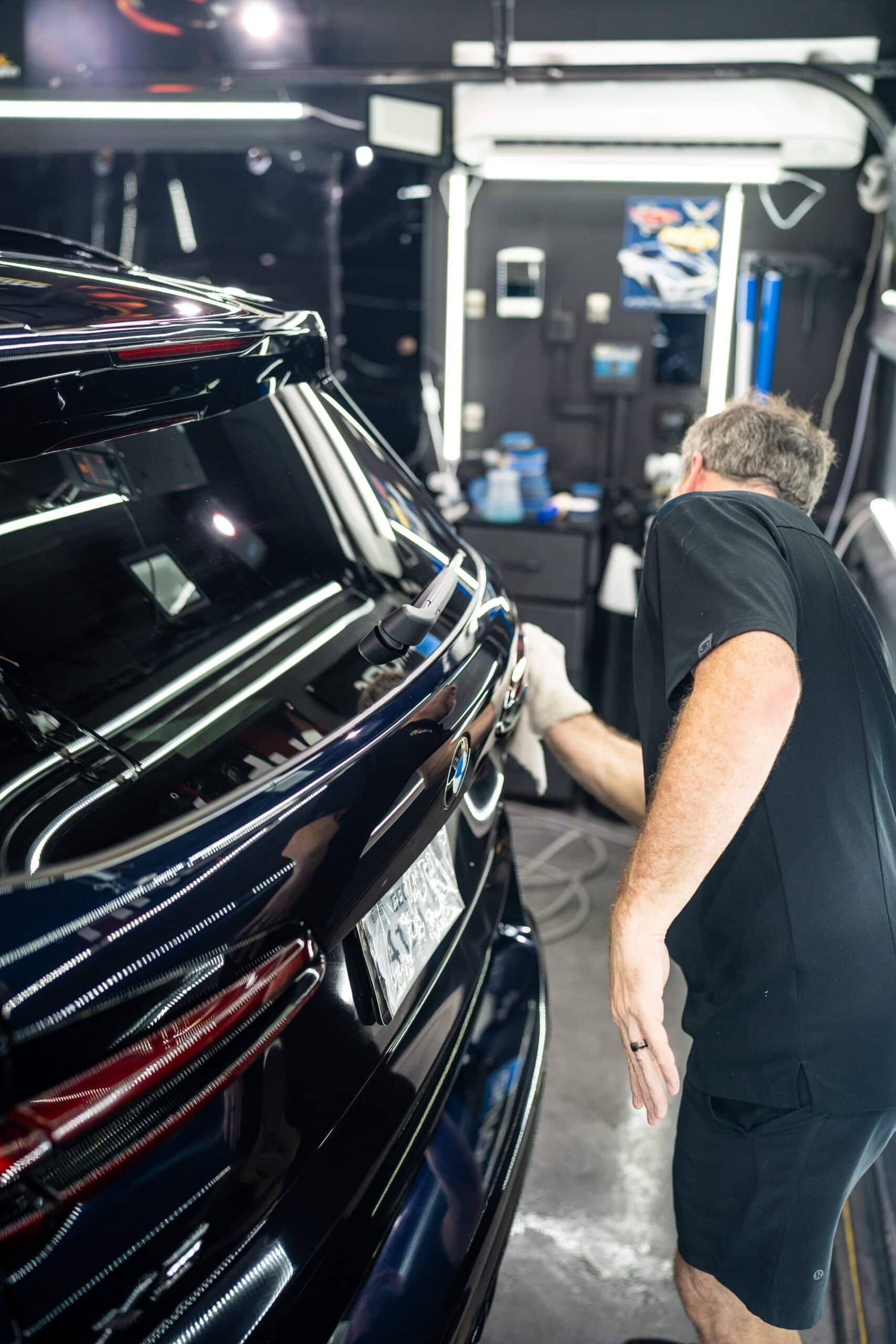 A man is polishing a black car in a garage.