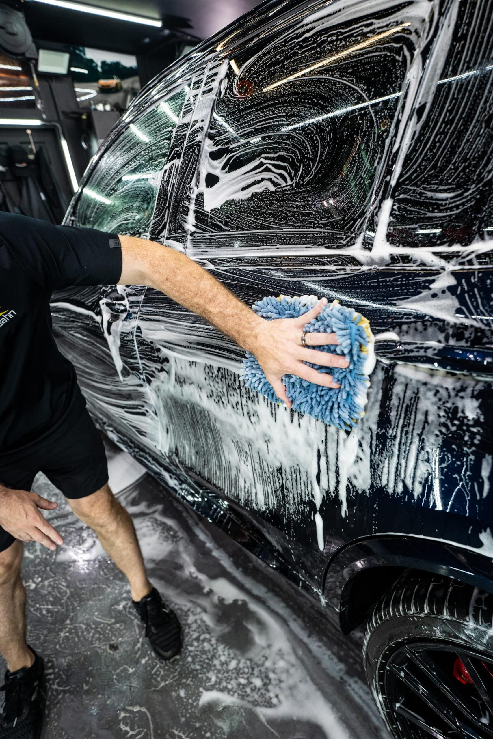 A man is washing a car with a blue sponge.