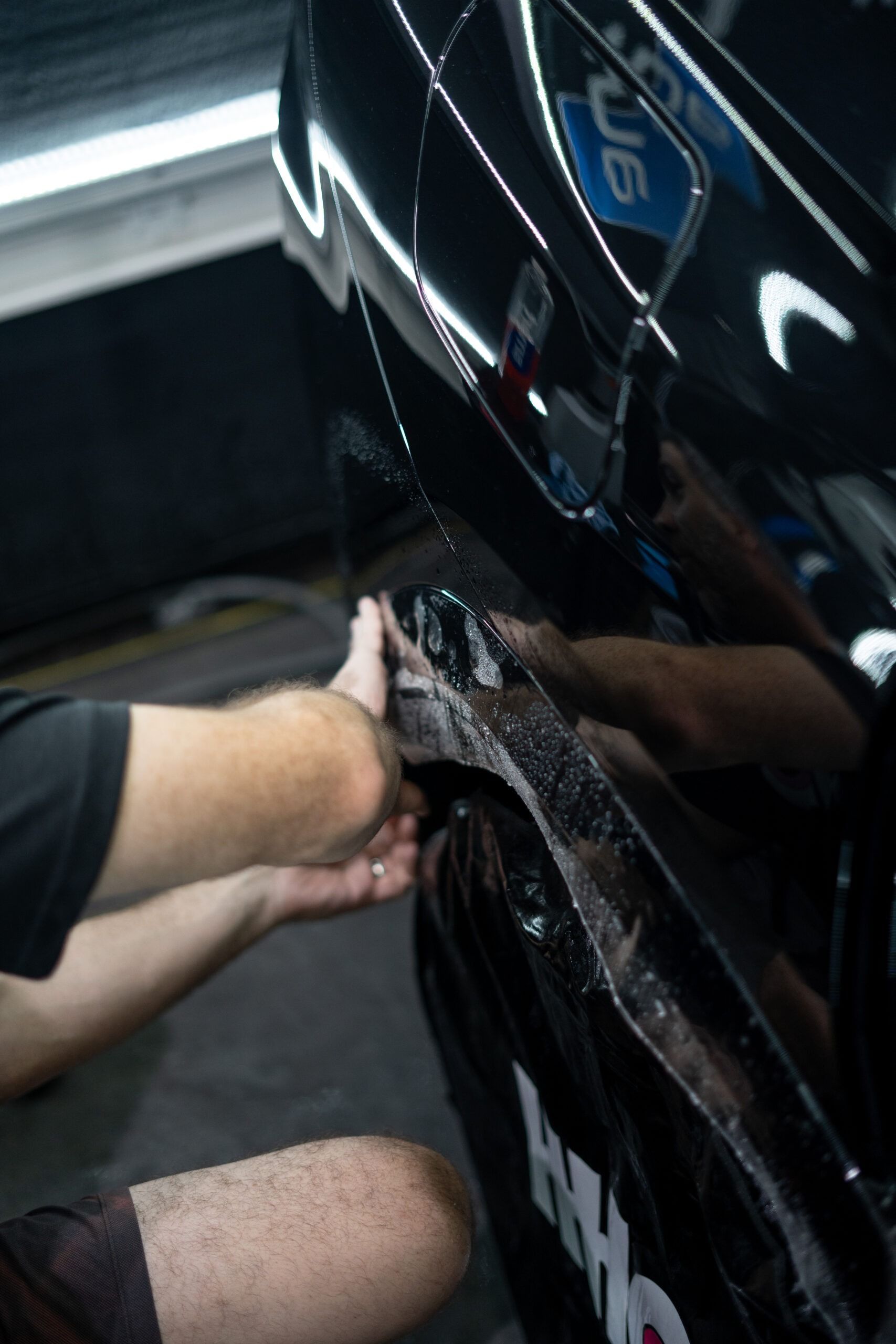 A man is applying a protective film to the side of a black car.