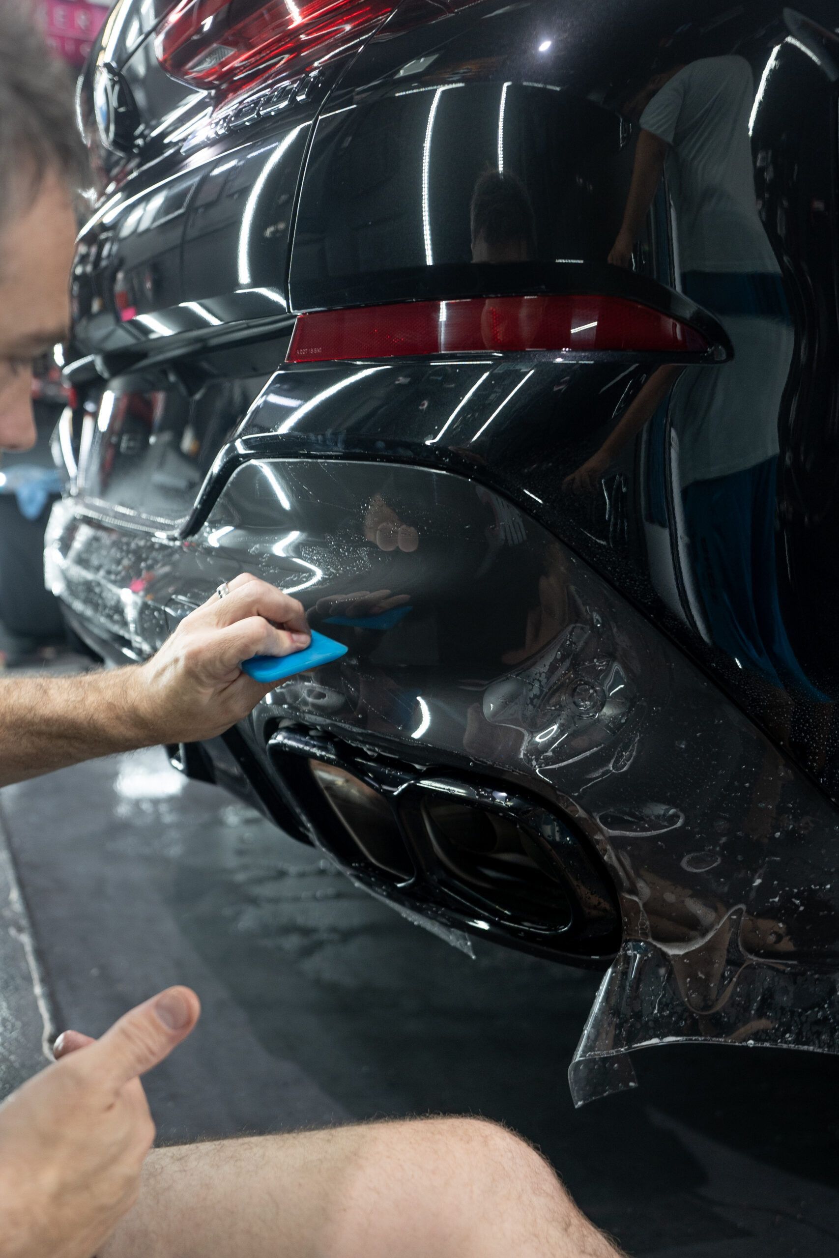 A man is applying protective film to the back of a car.