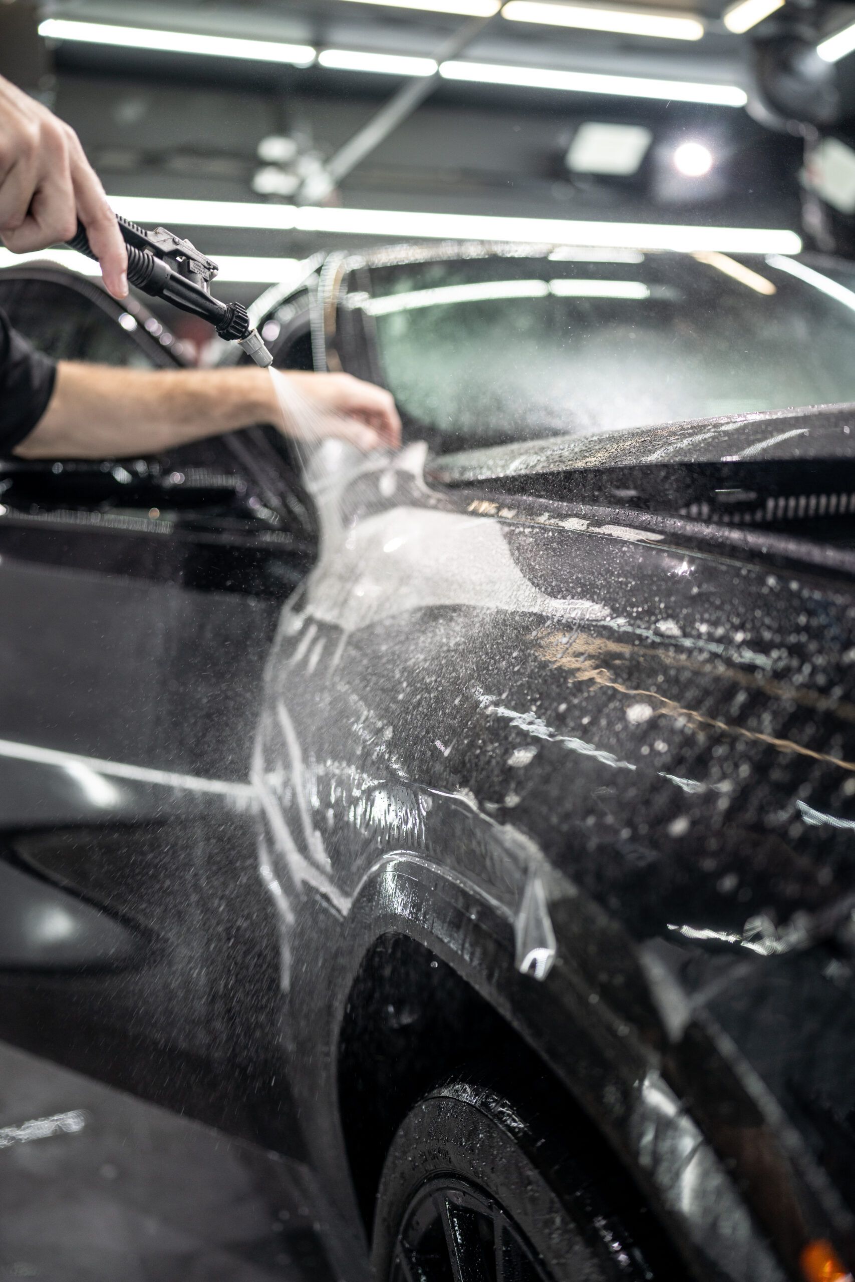A person is applying a protective film to a black car.