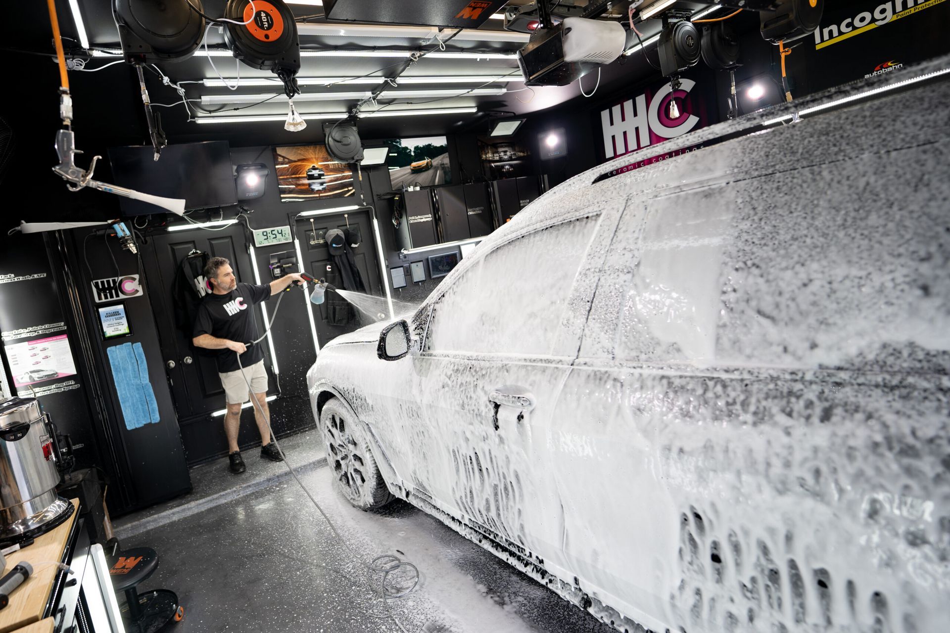 A man is standing next to a car covered in foam in a garage.