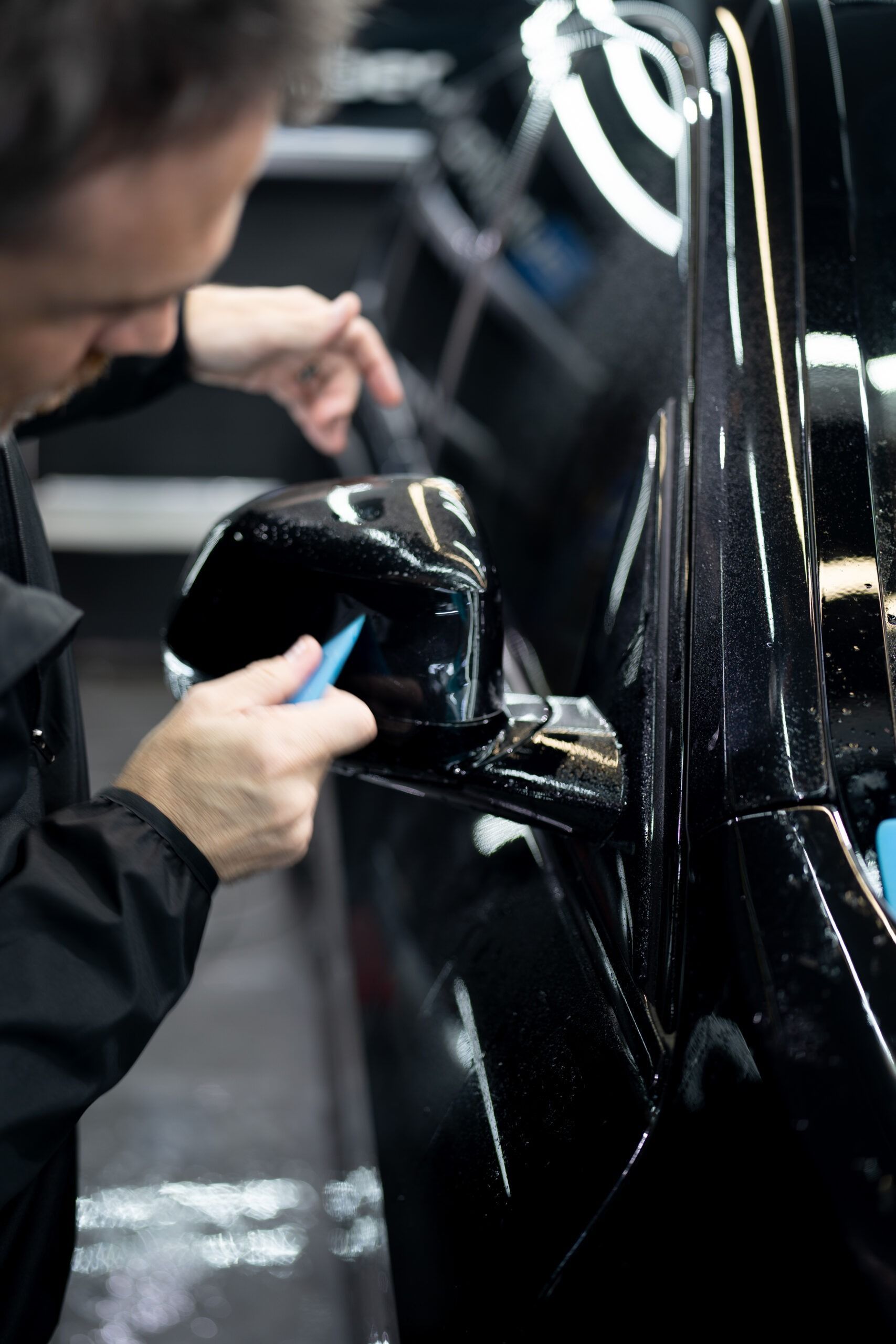 A man is cleaning the side mirrors of a black car.
