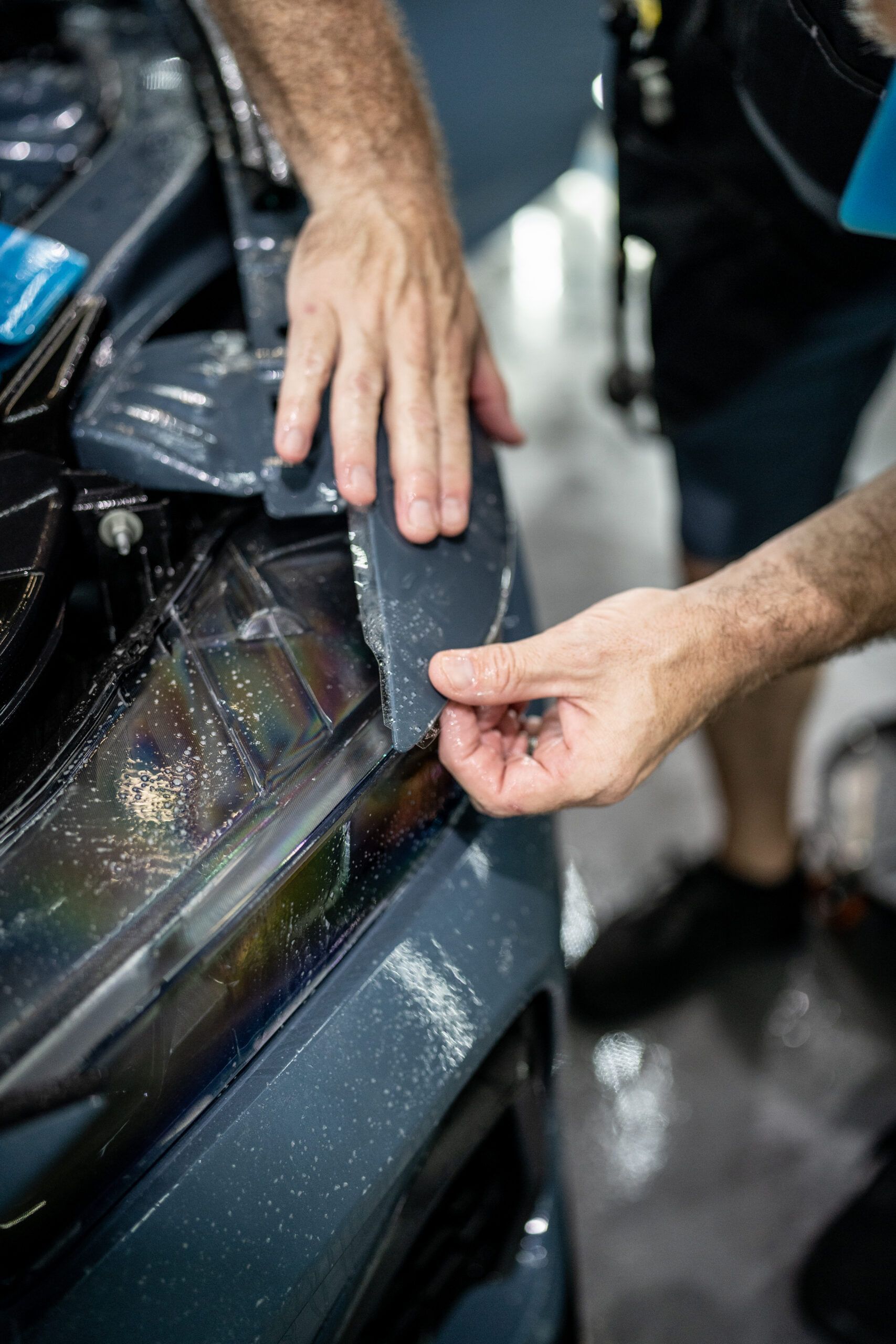 A man is applying a protective film to the headlight of a car.