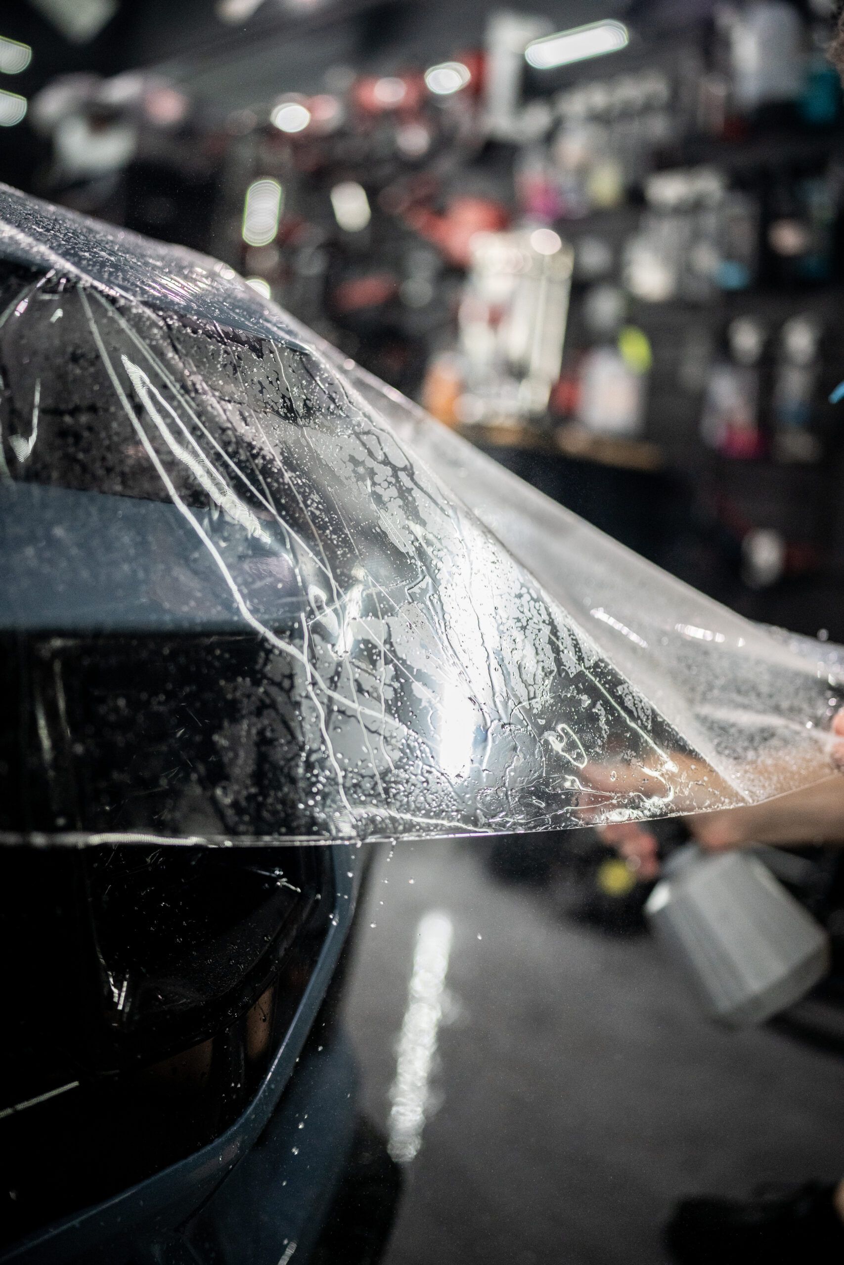 A person is wrapping a car with a clear plastic sheet.