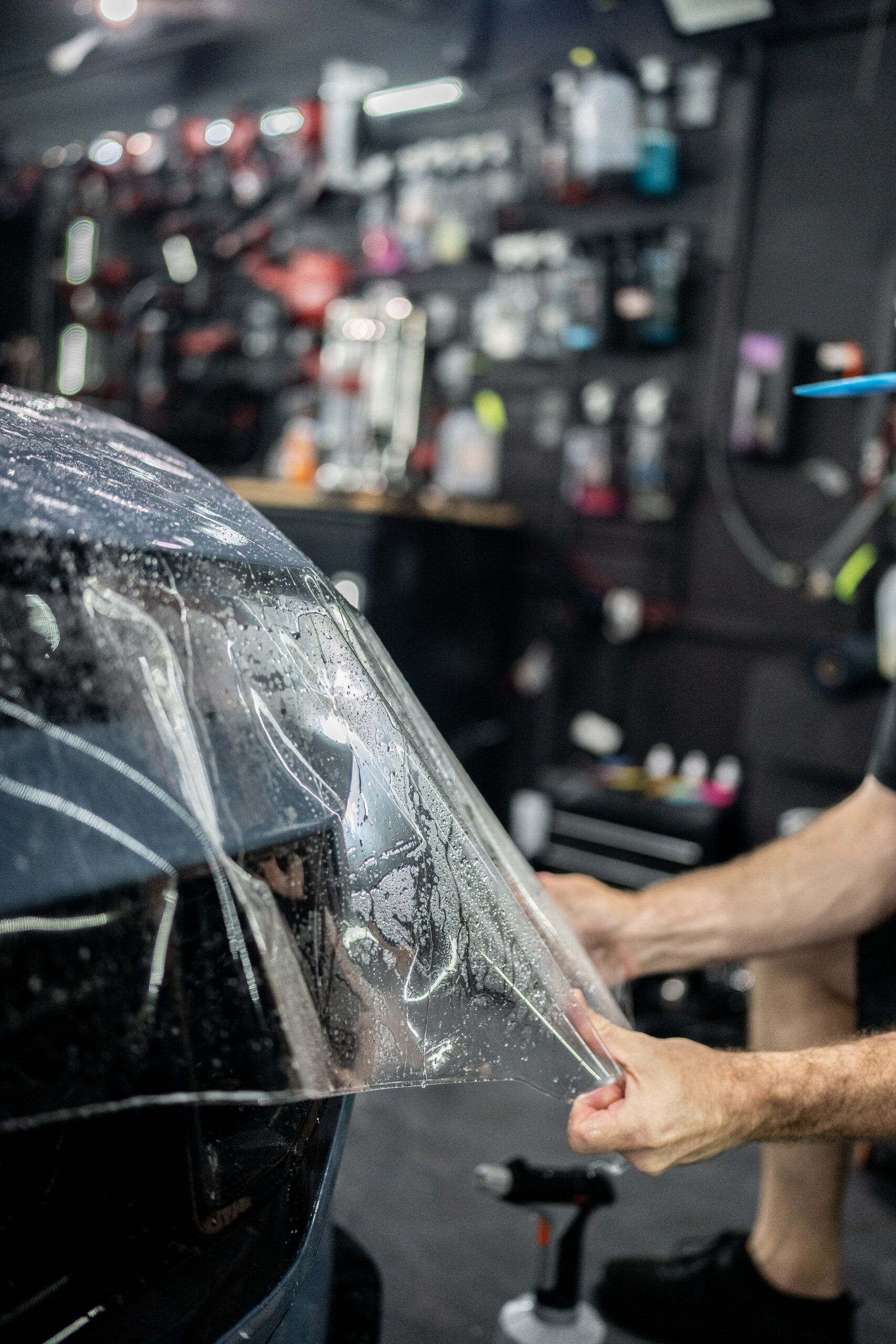 A man is applying a protective film to the windshield of a car.