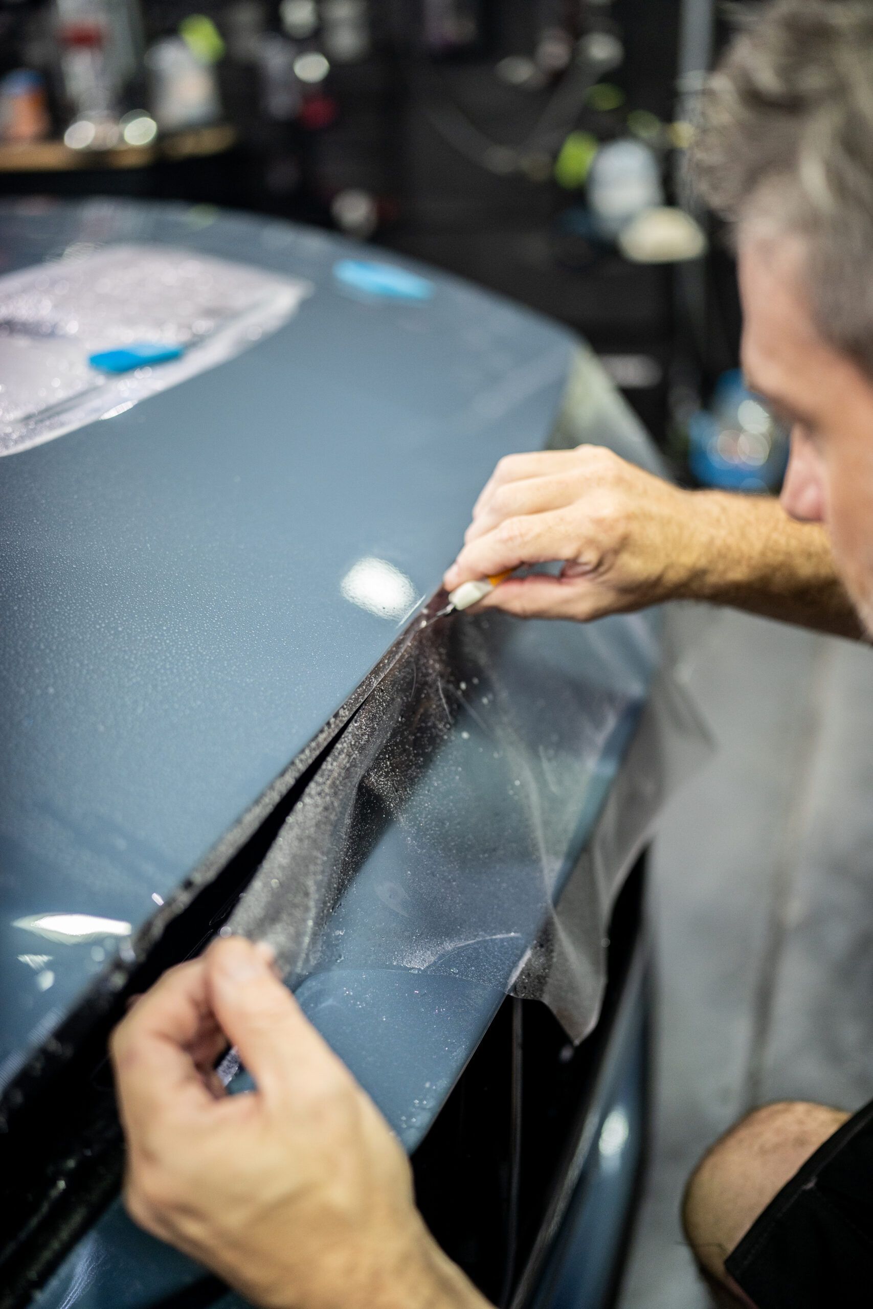 A man is applying a protective film to the hood of a car.