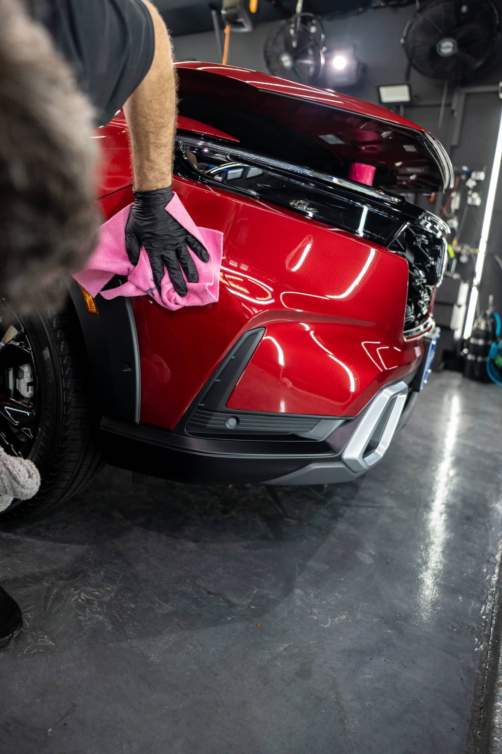 A man is cleaning a red car with a towel in a garage.
