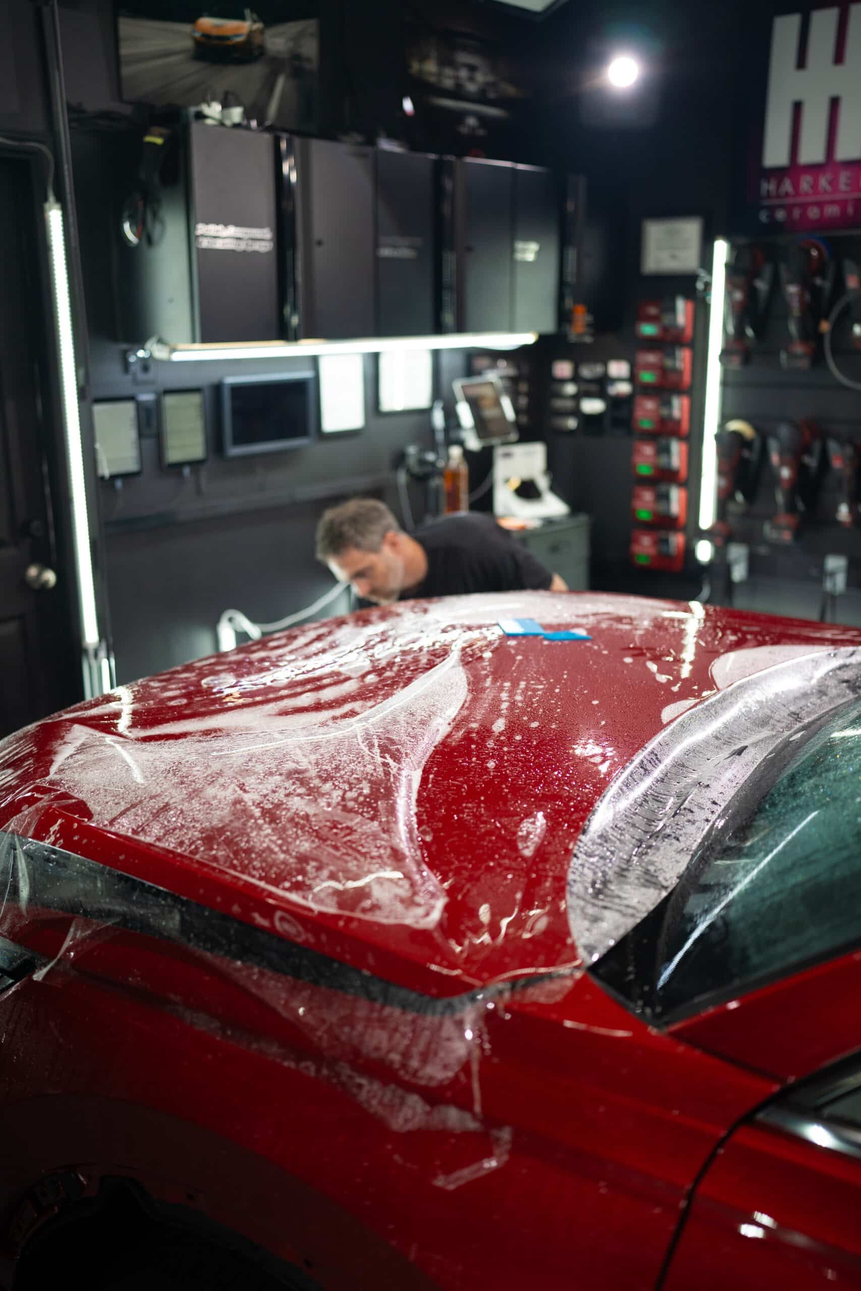 A man is working on the hood of a red car in a garage.