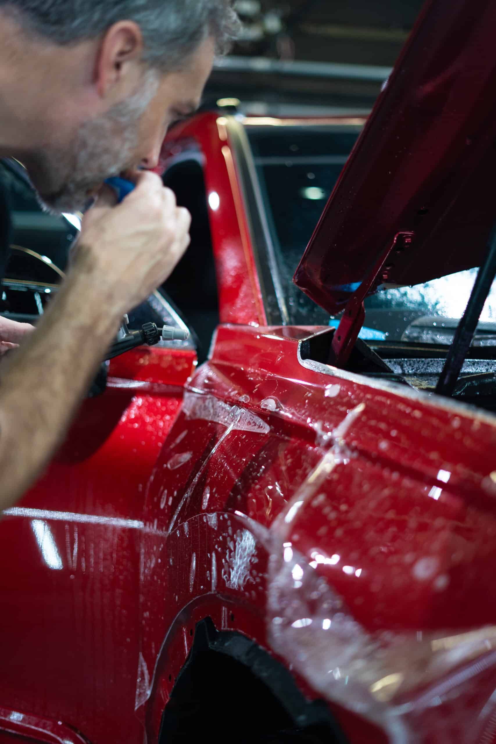 A man is wrapping a red car with plastic wrap.