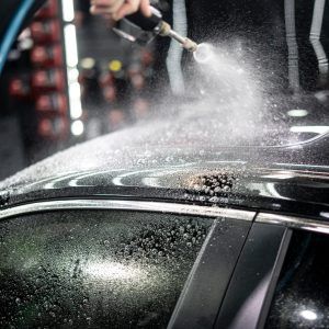 A person is spraying water on the roof of a car.