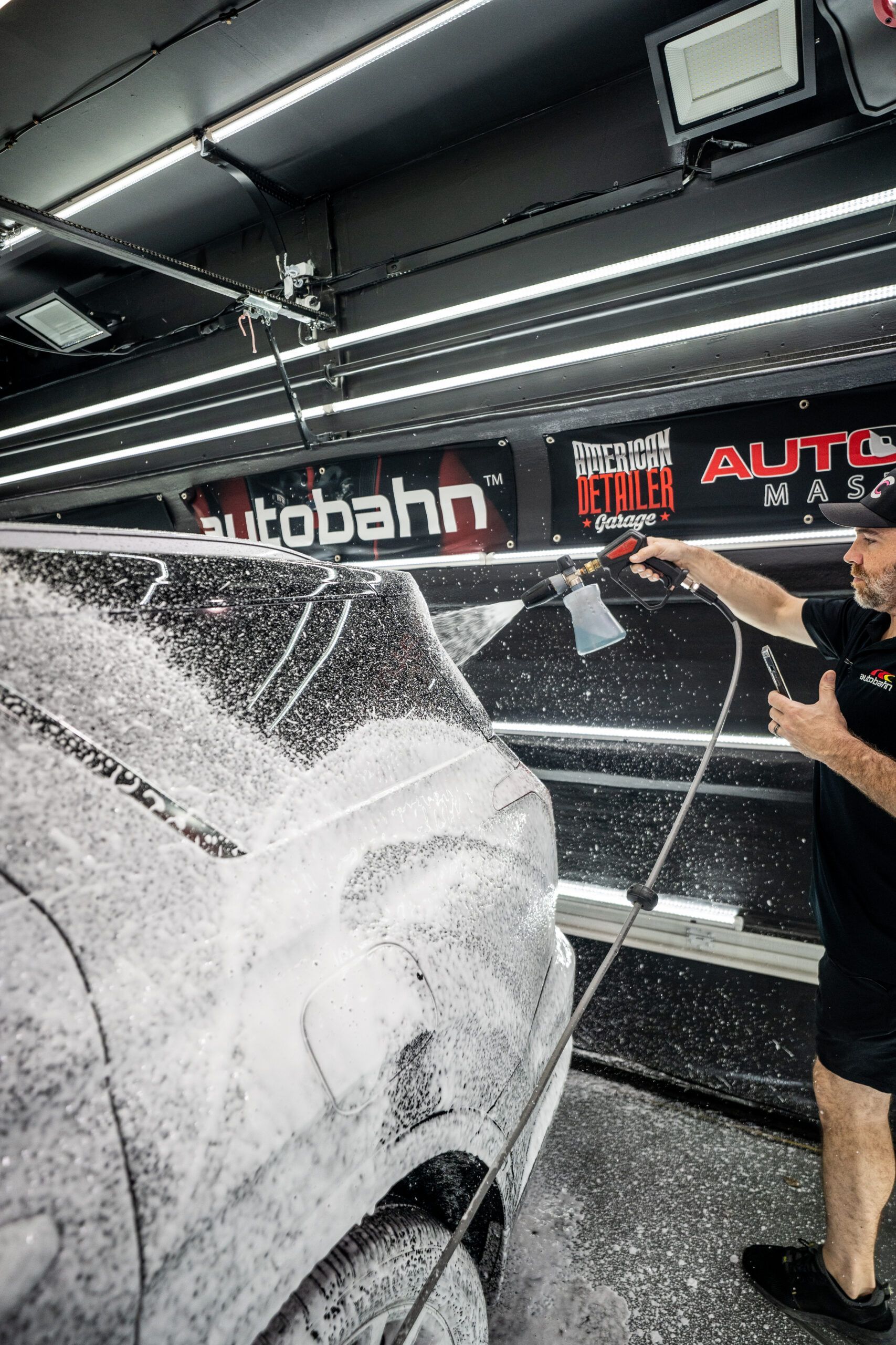 A man is washing a car with foam in a garage.