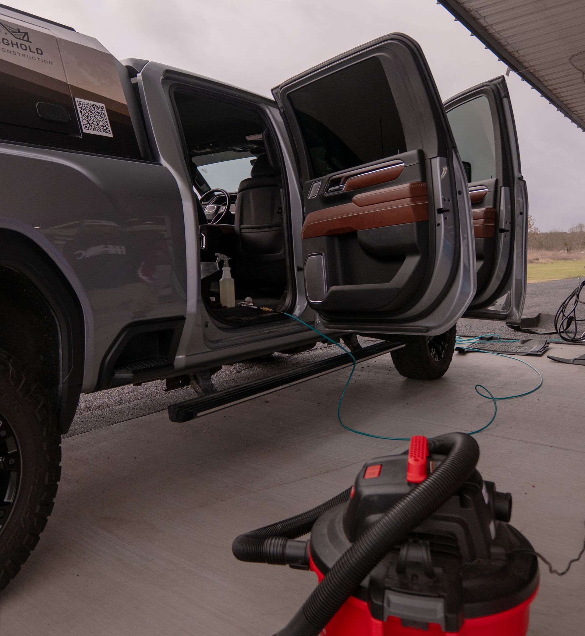 Person cleaning a car door interior with a spray gun and blue microfiber cloth.