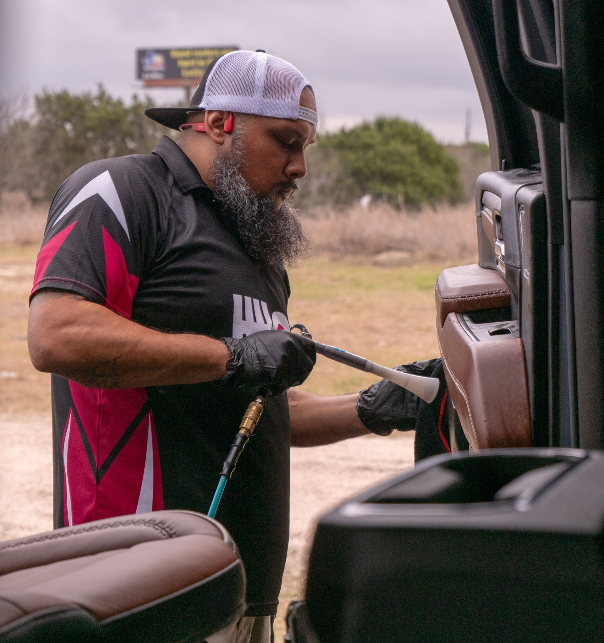 Person wearing black gloves cleaning car door interior with red tool and cloth.