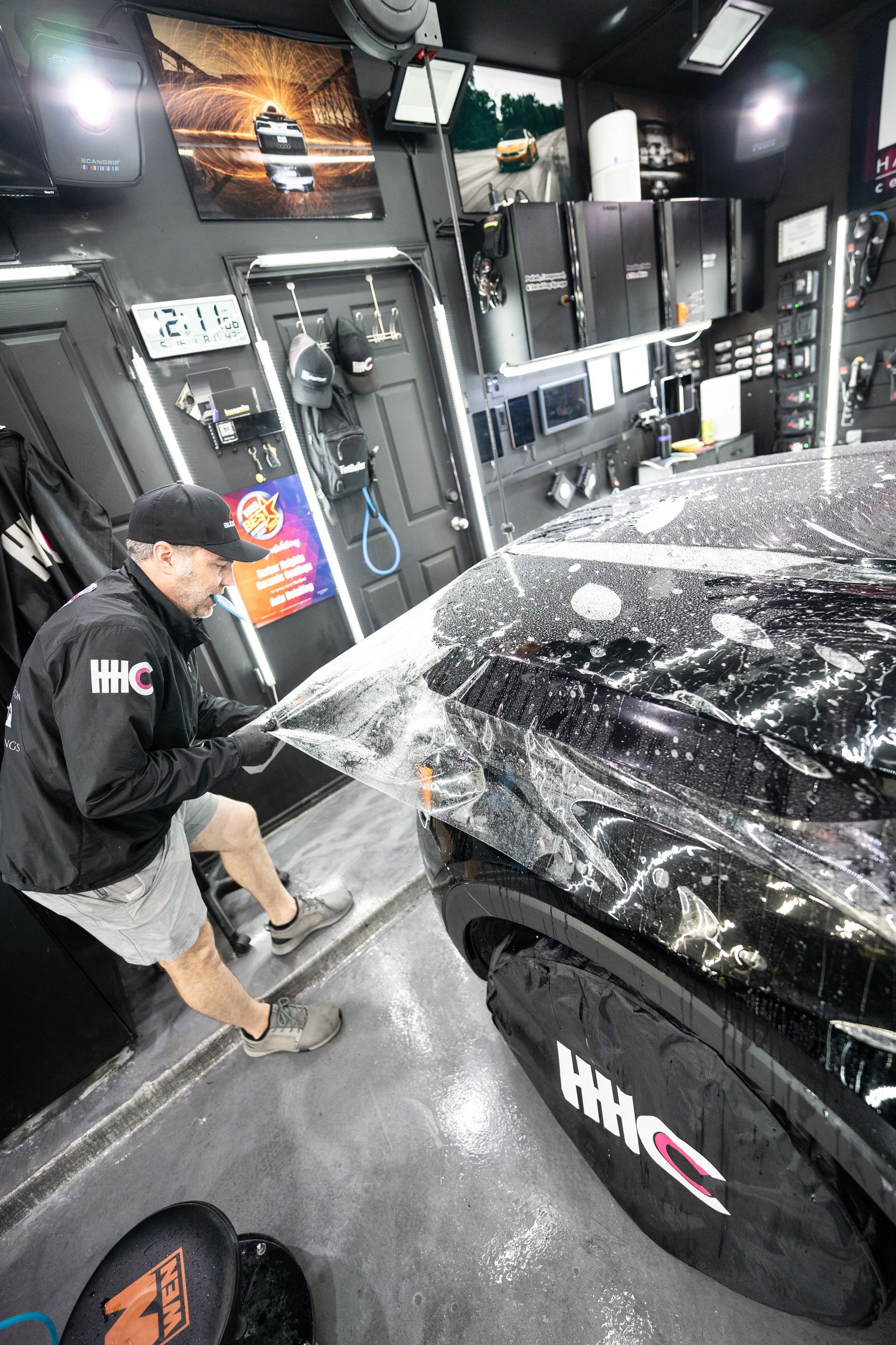 A man is wrapping a car with plastic wrap in a garage.