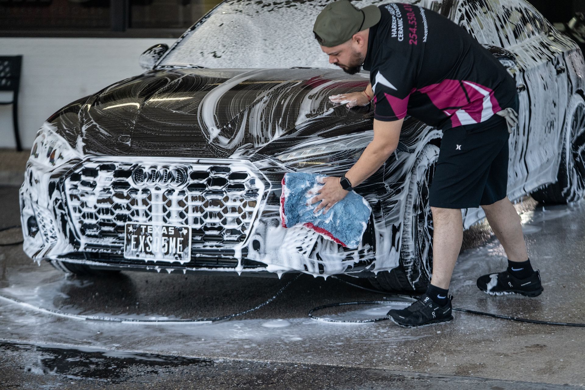 Man washes a black car, using a soapy cloth, outdoors at a car wash.