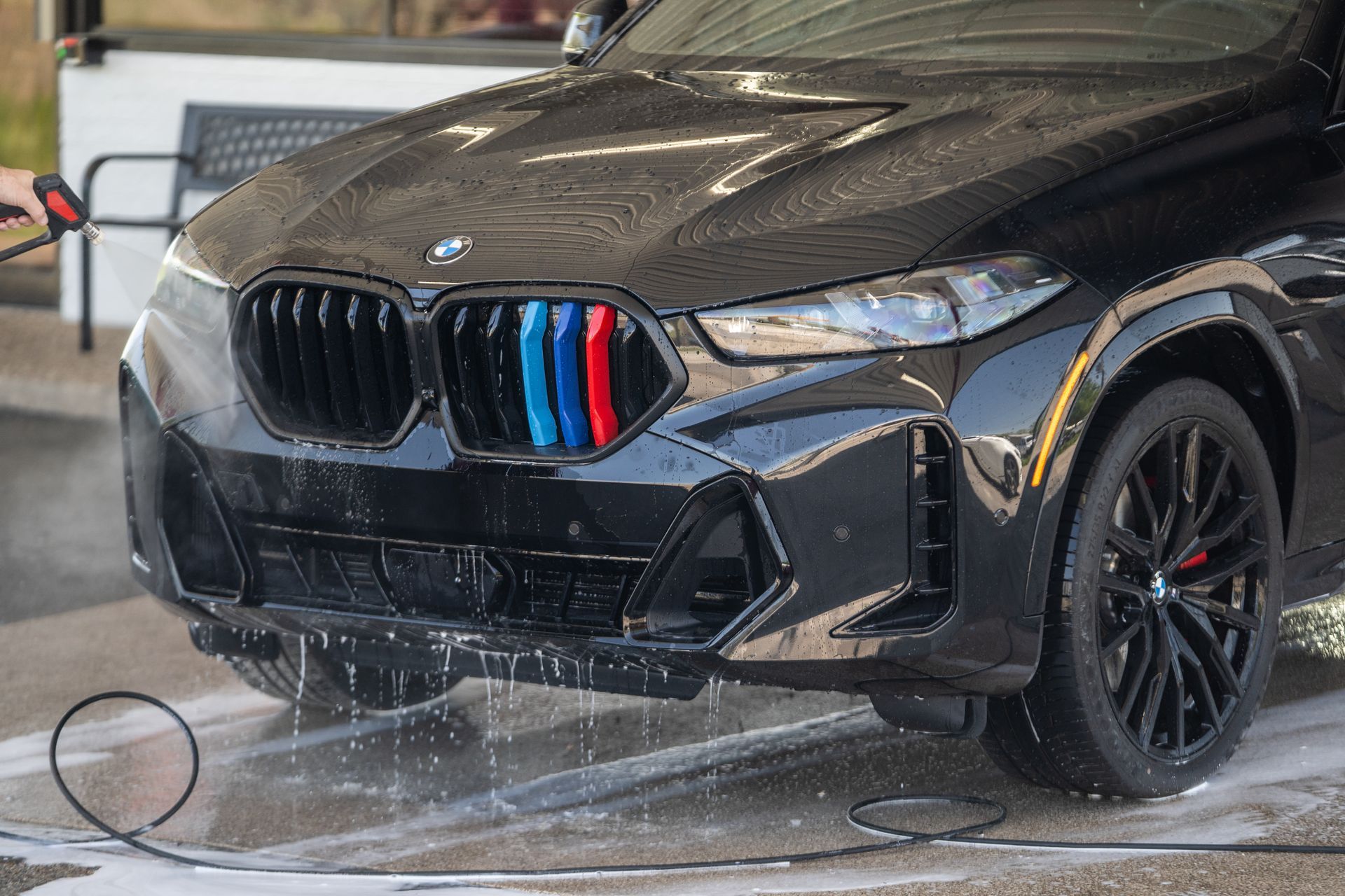 Black BMW SUV being washed with a pressure washer; blue, red, and light blue on grill.